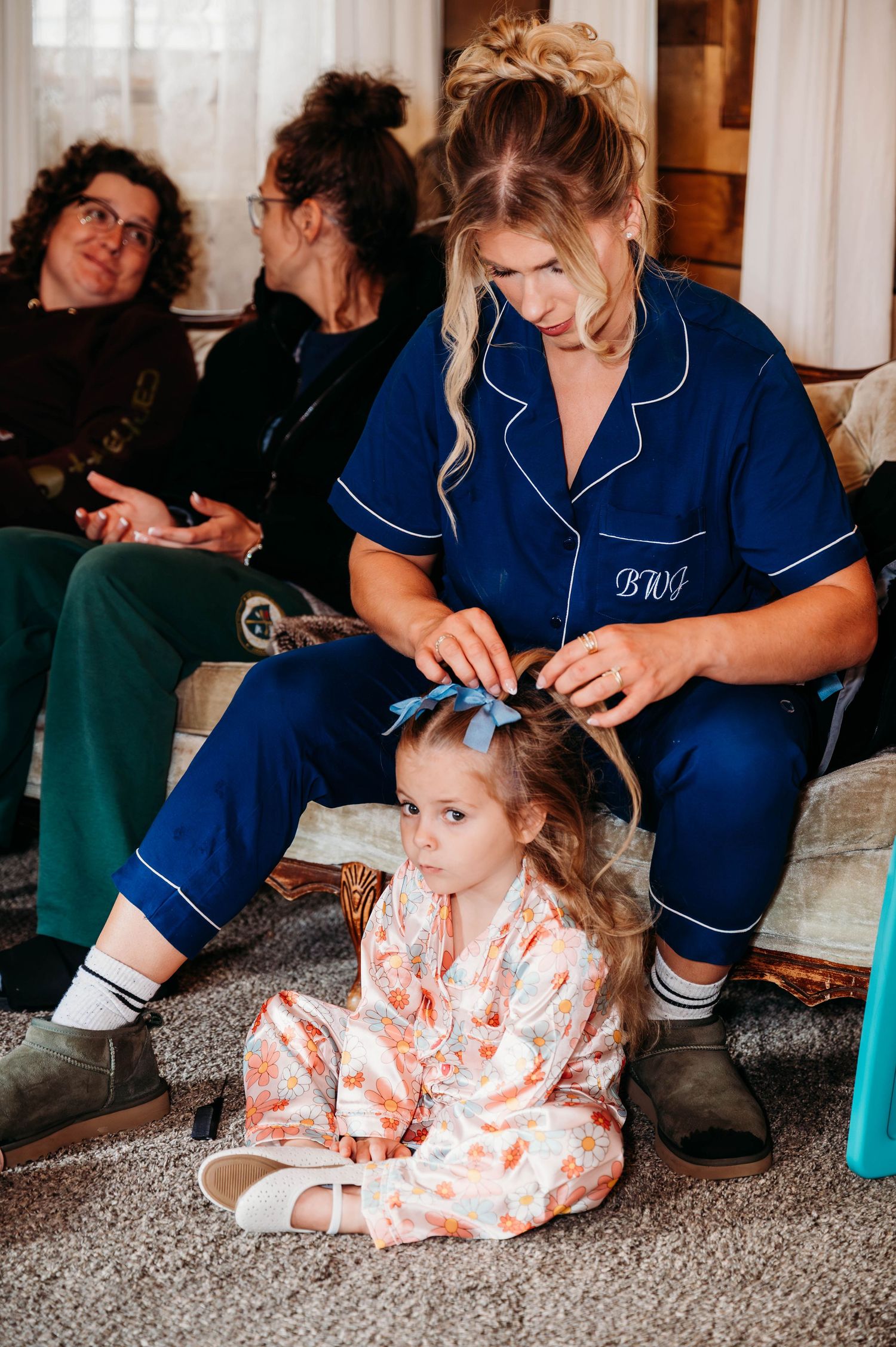 A child in a floral robe sits on carpet while healthcare workers in blue scrubs attend to them during a medical visit.