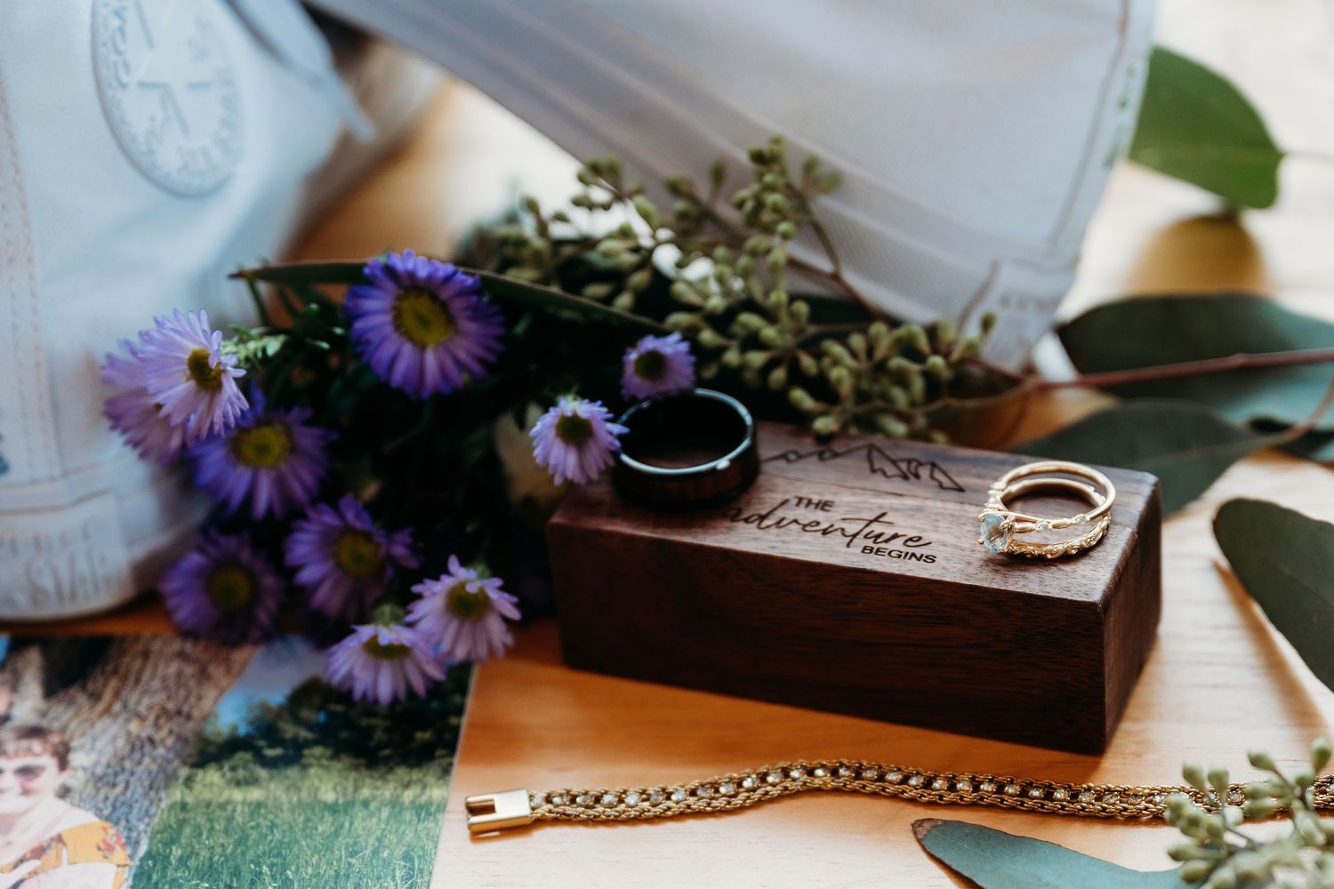 Vintage teacup and purple aster flowers arranged with antique books and decorative items on rustic wooden surface.