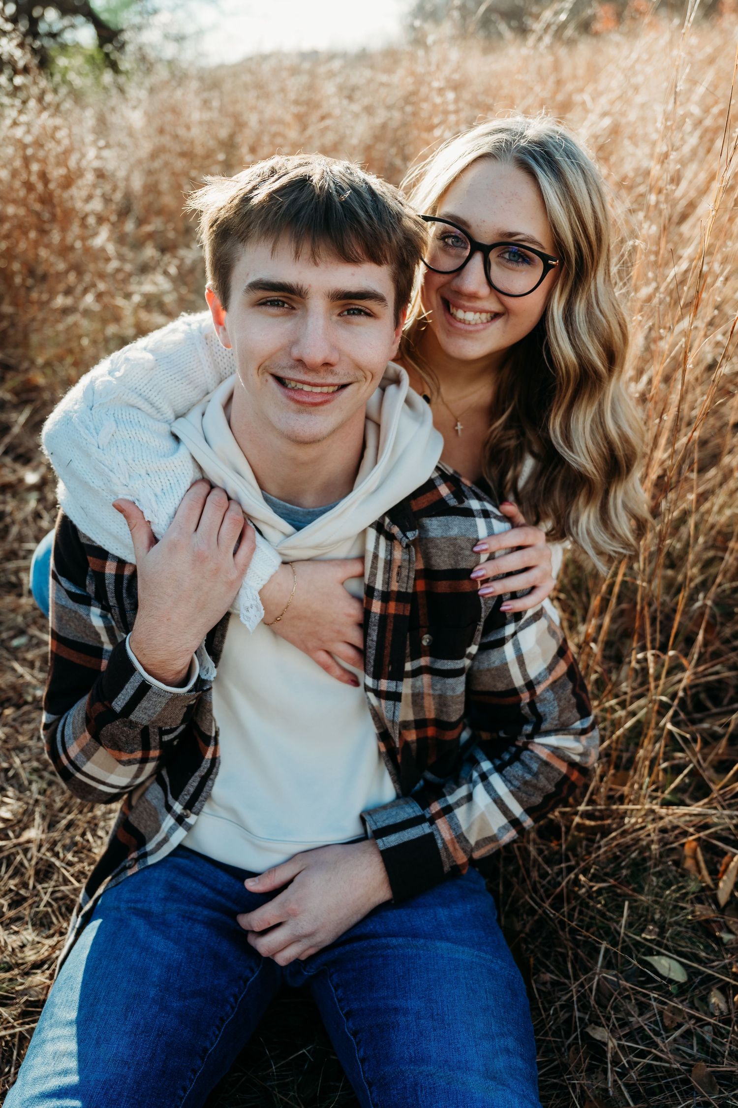 A couple shares playful moments together in a field of tall grass during a golden hour photoshoot.