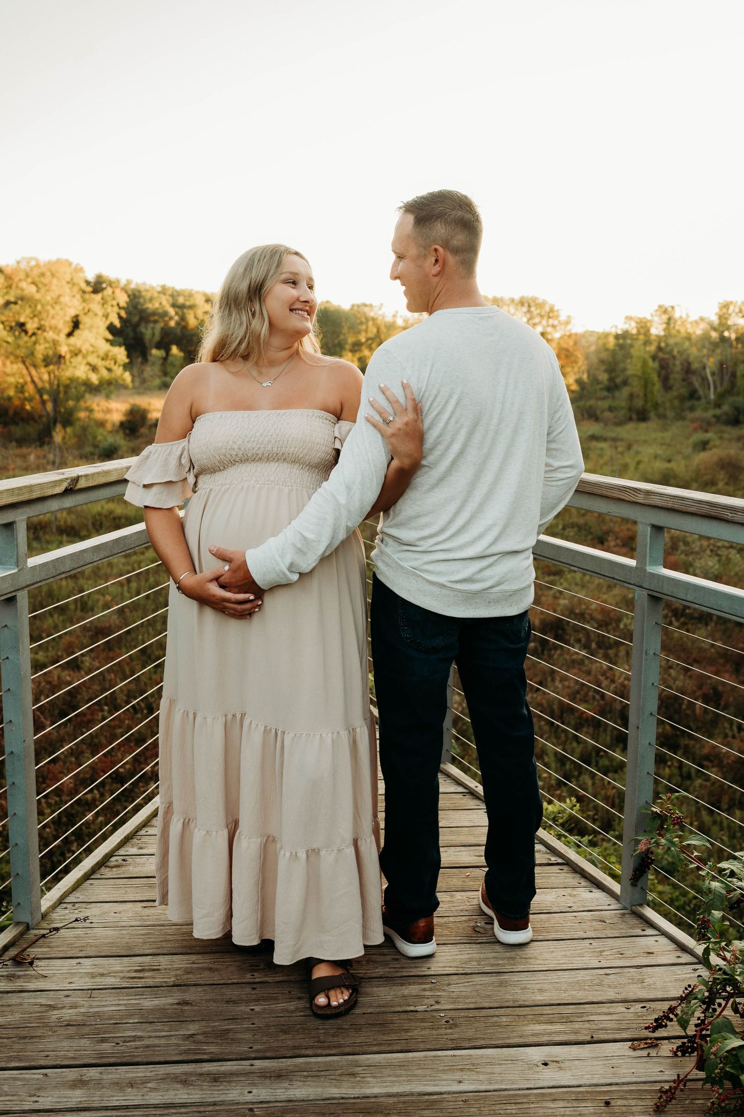 A couple walks along a wooden deck at sunset holding hands and smiling in romantic engagement photos.