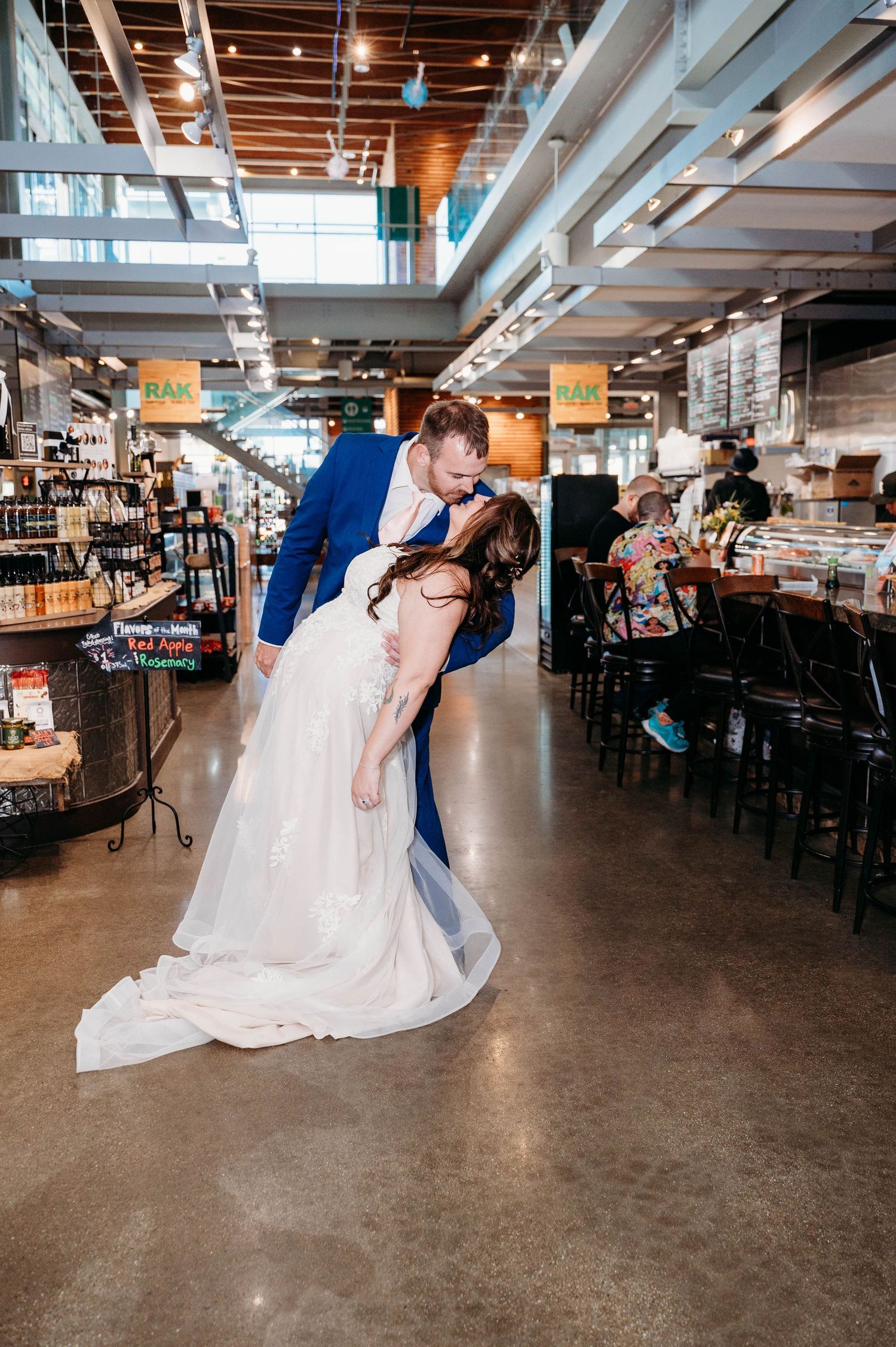 Romantic dip kiss between couple in formal wedding attire inside an industrial-style venue with exposed ceiling.