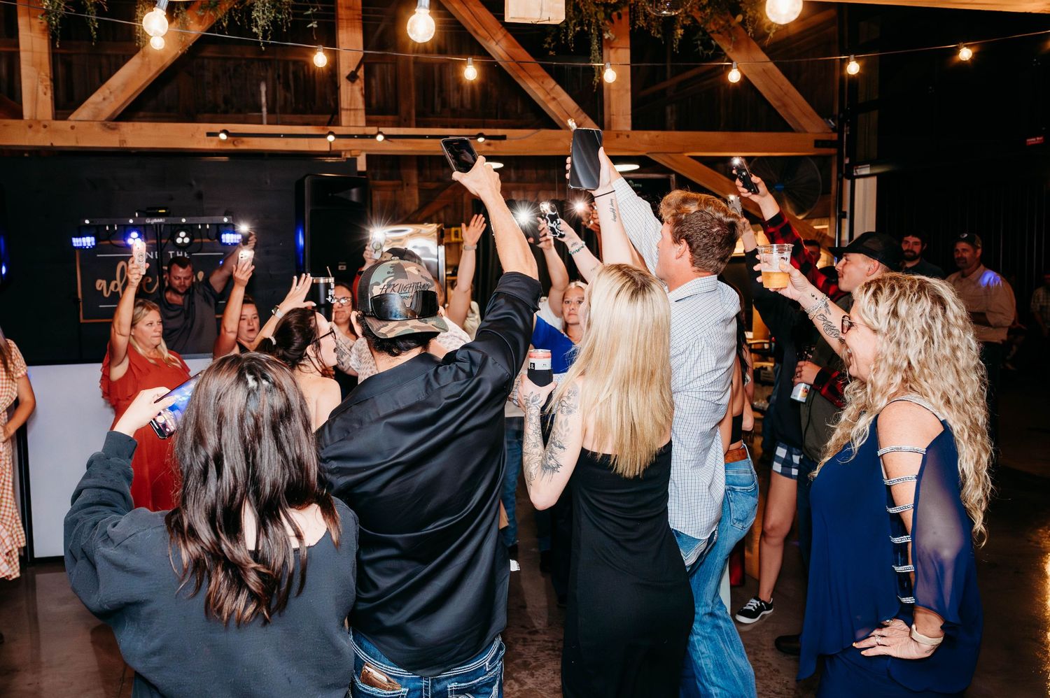 People dancing and celebrating at a lively party venue with warm overhead lighting and exposed wooden beams.