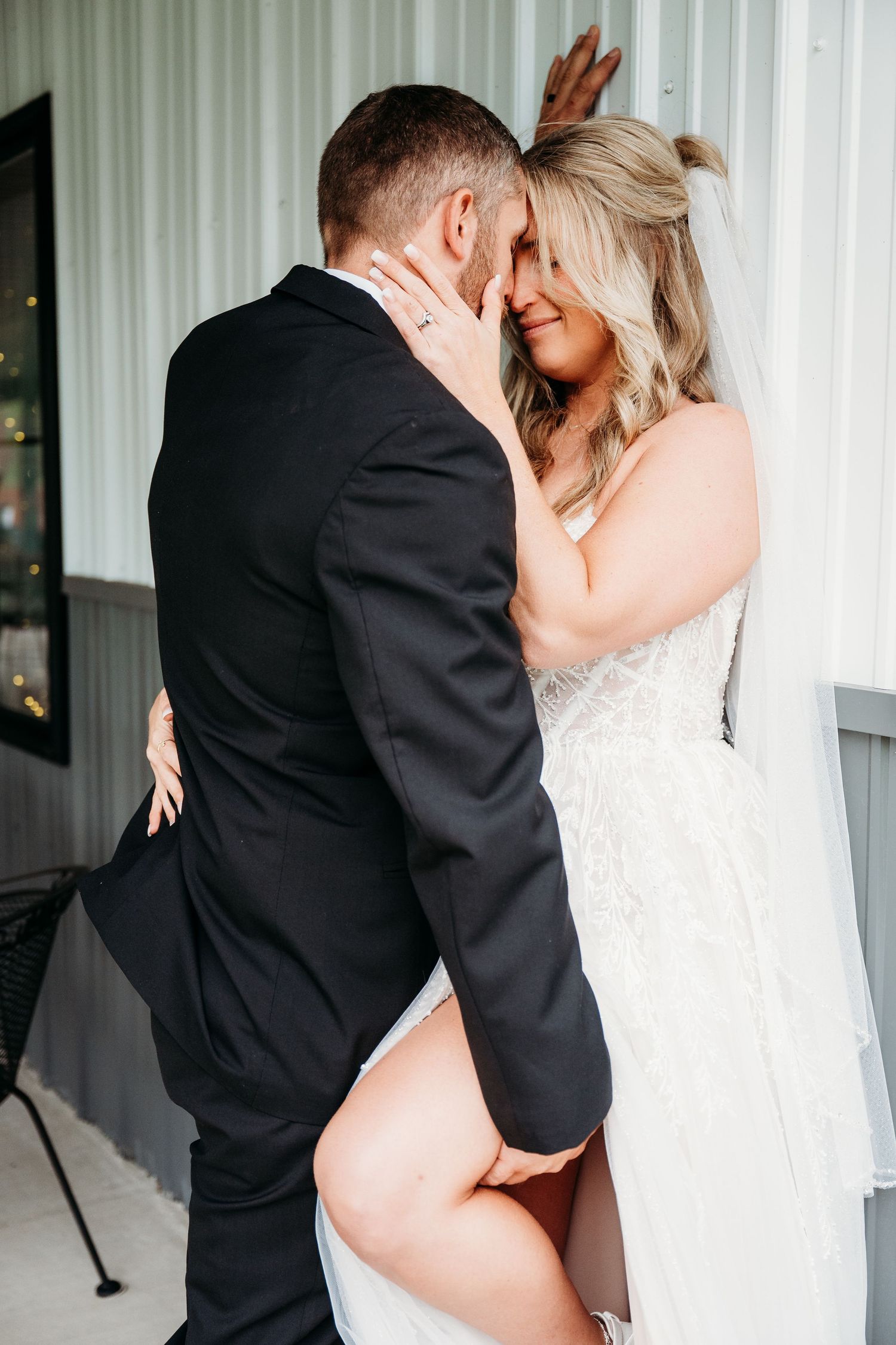 Bride and groom sharing an intimate moment, bride in lace wedding dress with veil embracing her groom.