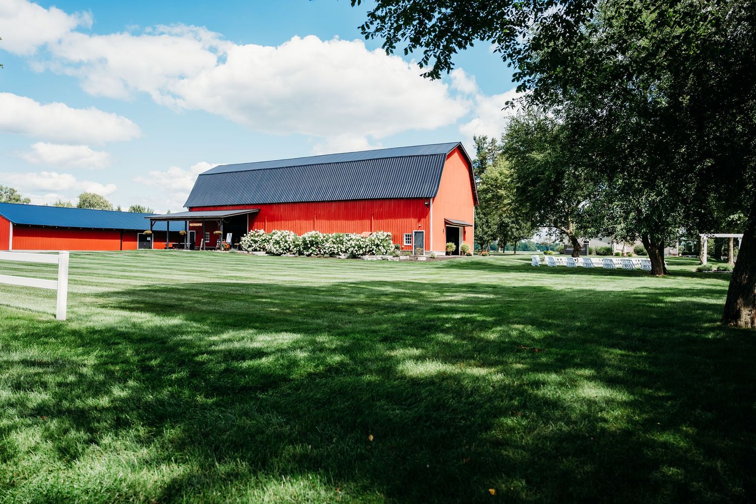 Panoramic view of a red barn and green pastures under a bright blue sky with scattered white clouds.