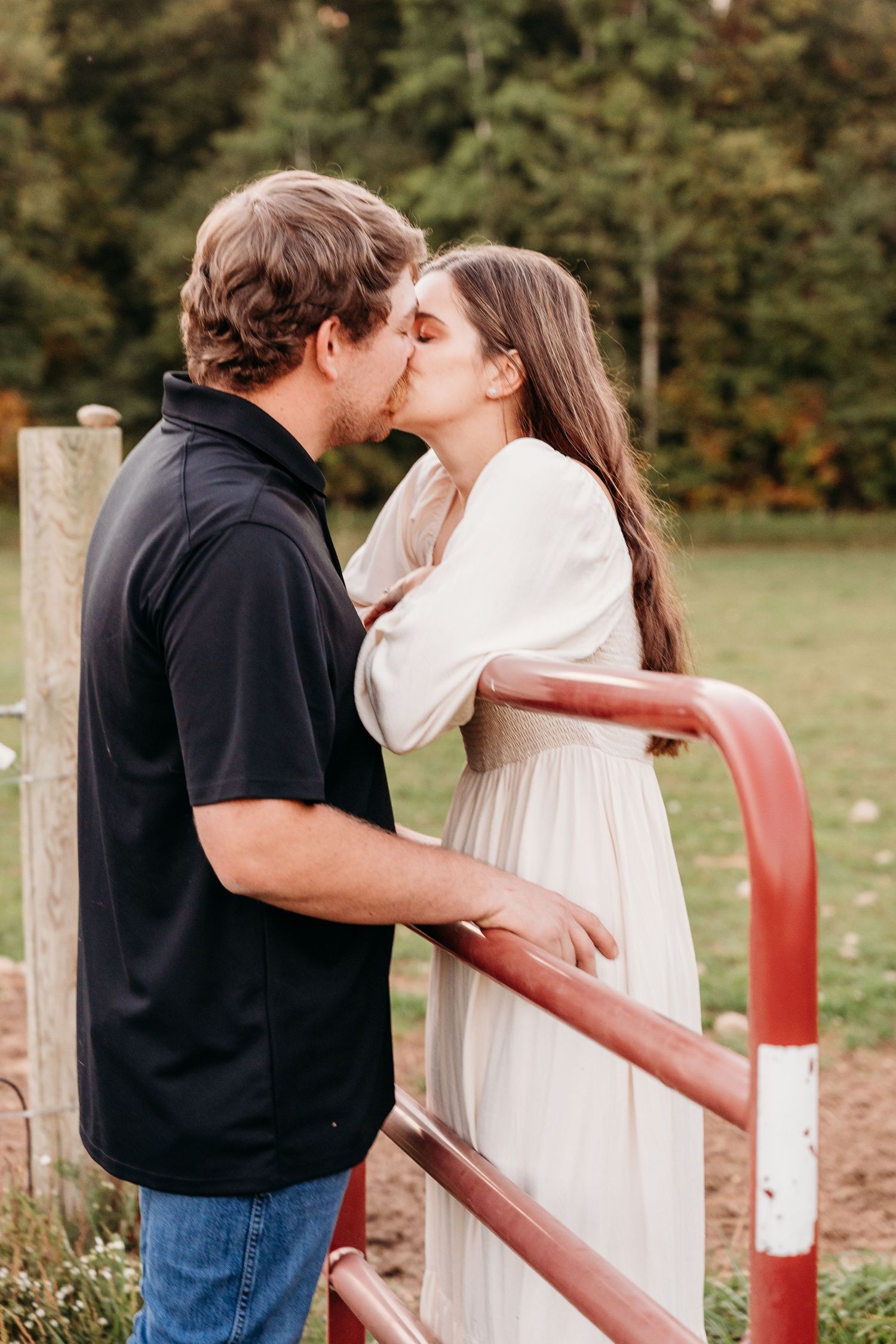 Couple embracing by a rustic wooden fence in an outdoor setting.