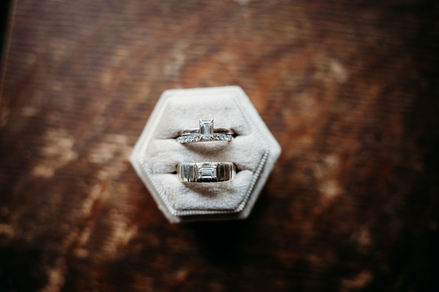 Two elegant engagement rings nestled in a white hexagonal ring box on a rustic wooden surface.