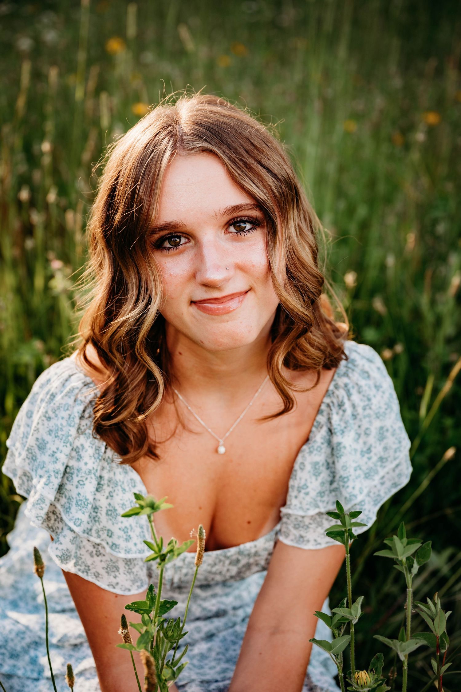 Young woman in floral dress smiling in a wildflower field.