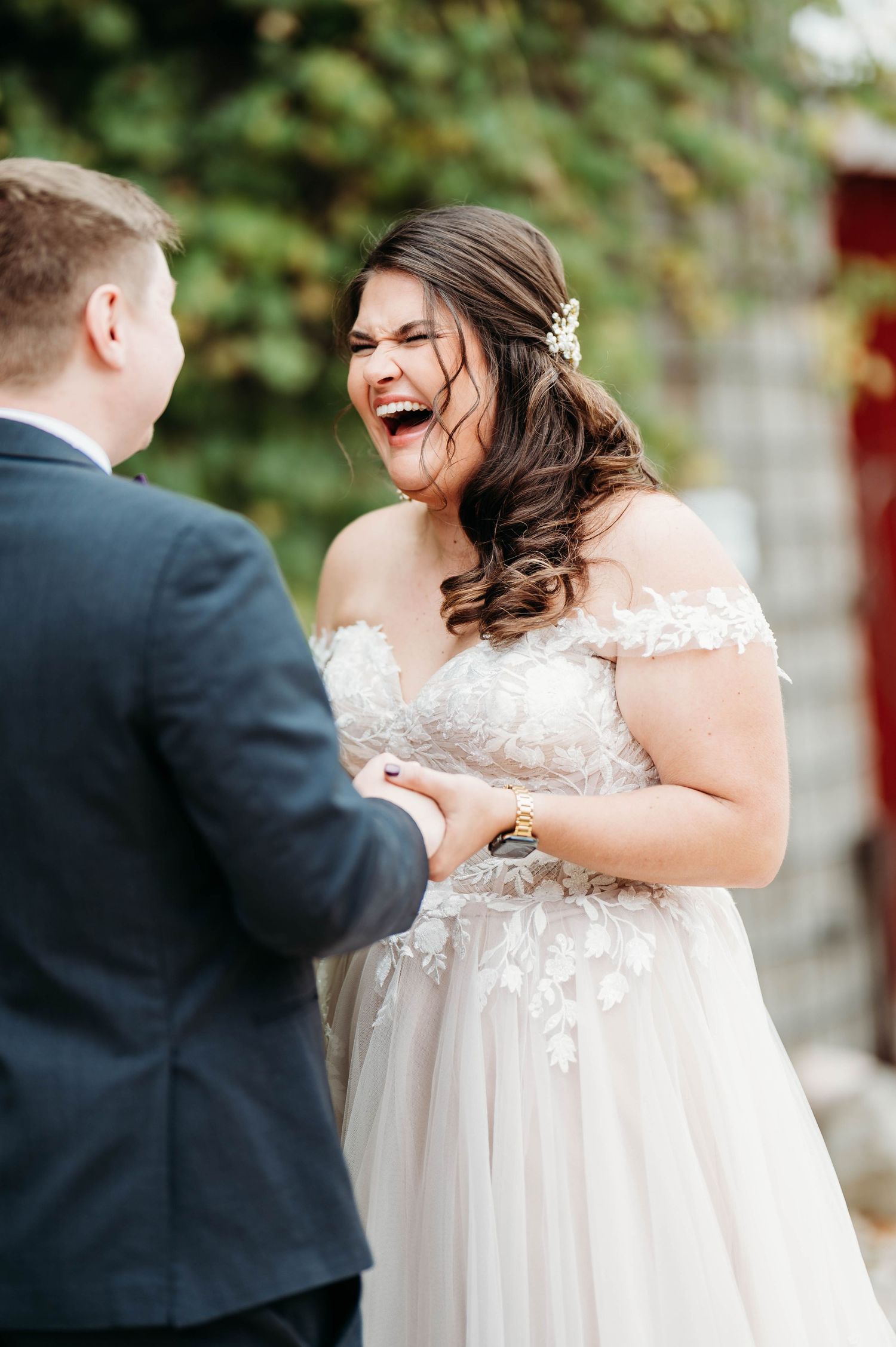 Bride in lace wedding gown shares joyful moment during first look with groom outdoors.