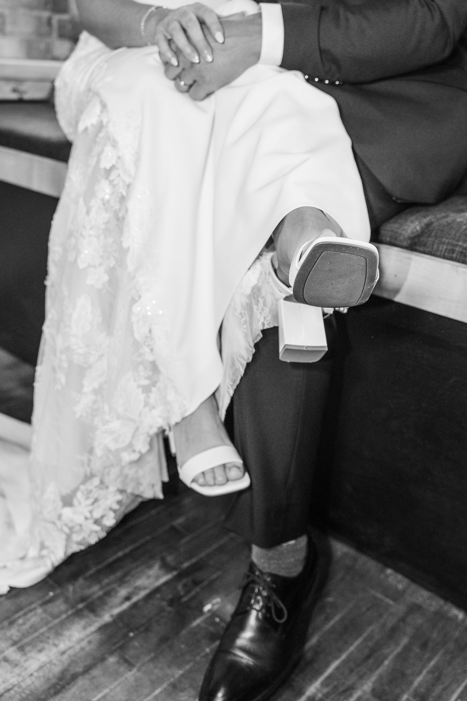 Close-up of bride and groom's feet sitting together on wooden bench showing formal wedding attire.