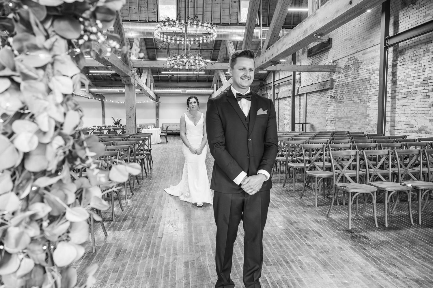 Black and white photo of a first look moment at a rustic venue with wooden floors and vintage metal chairs.