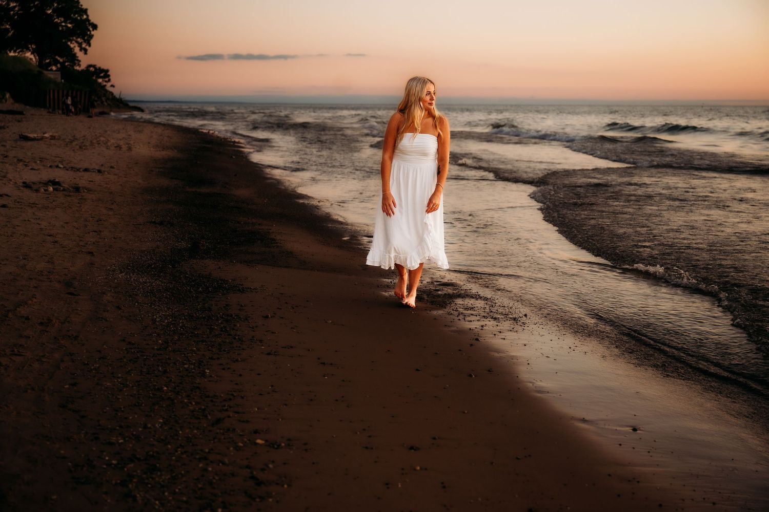 Beach photoshoot at golden hour with footprints in the sand and ocean waves in the background.