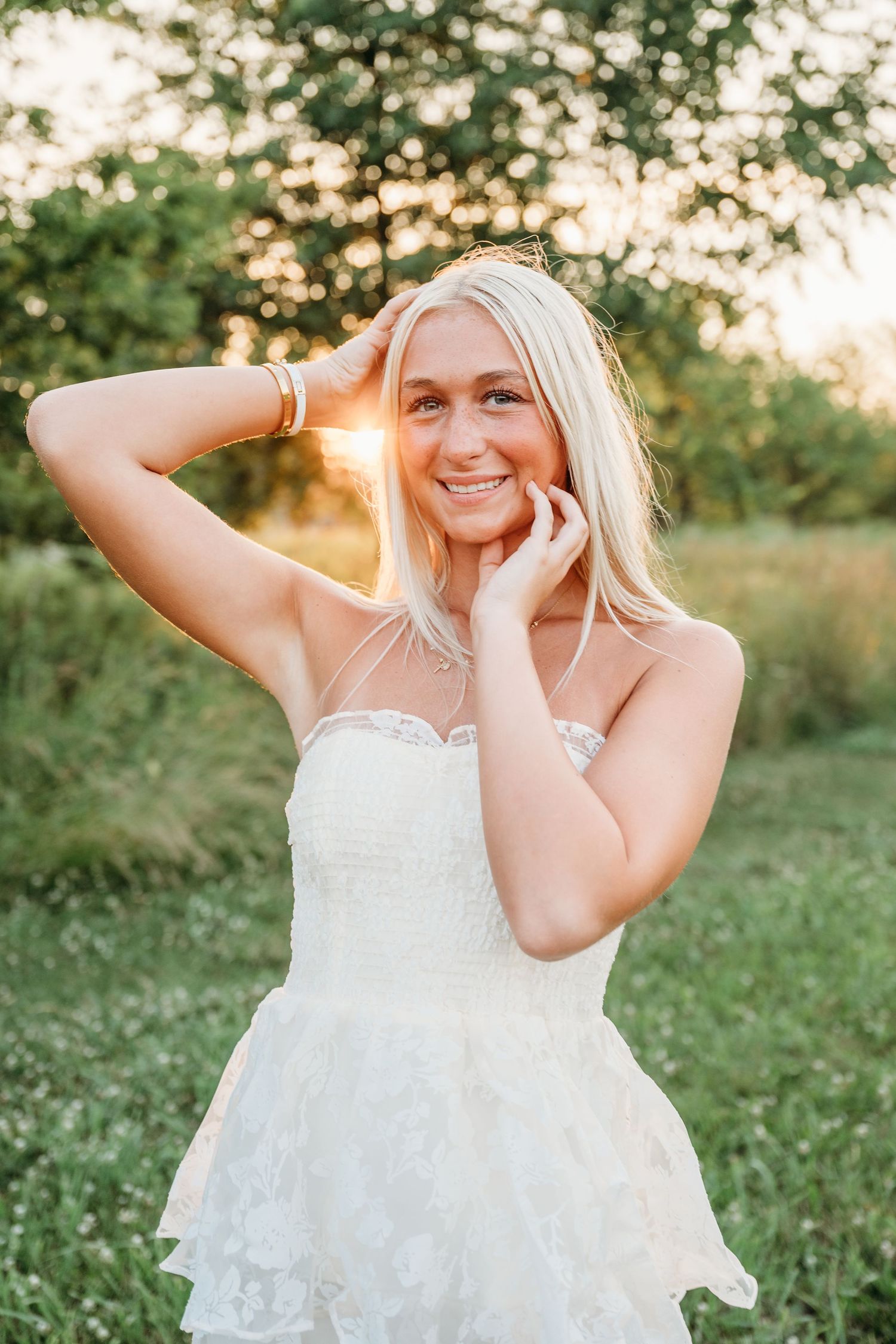 Playful summer portrait session in a grassy field with golden sunlight and a white lace dress.