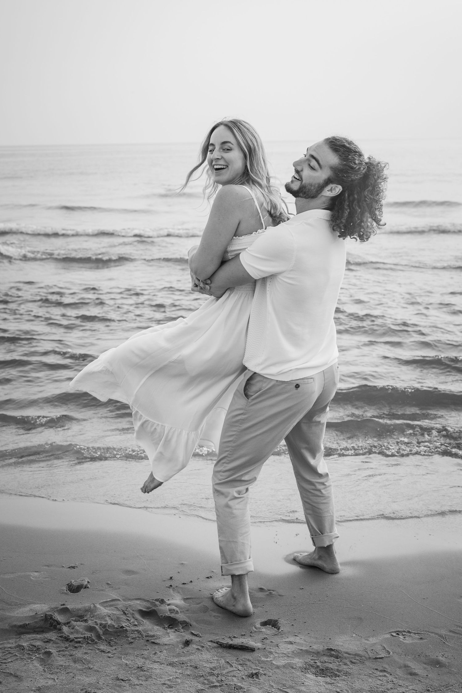 A couple sharing a joyful moment while dancing barefoot on the beach with waves in the background.