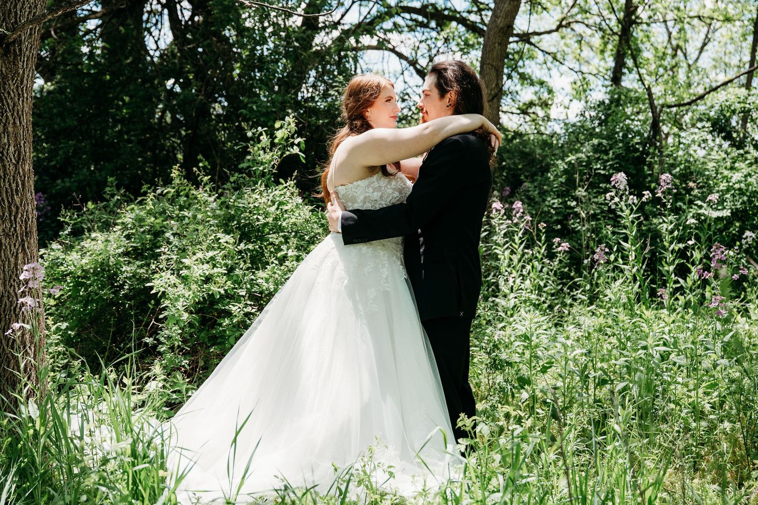 A romantic outdoor wedding couple shares a tender embrace in a lush green wooded setting.