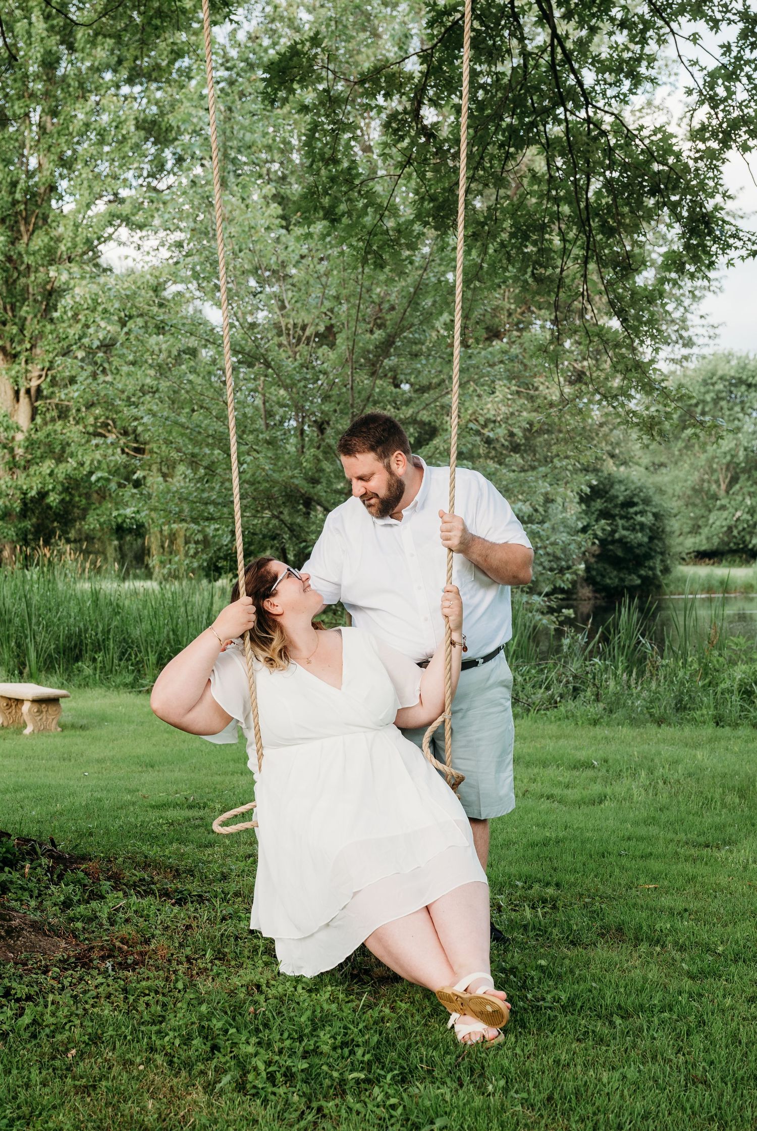 A couple shares a romantic moment on a tree swing in a lush green garden setting during a summer photoshoot.