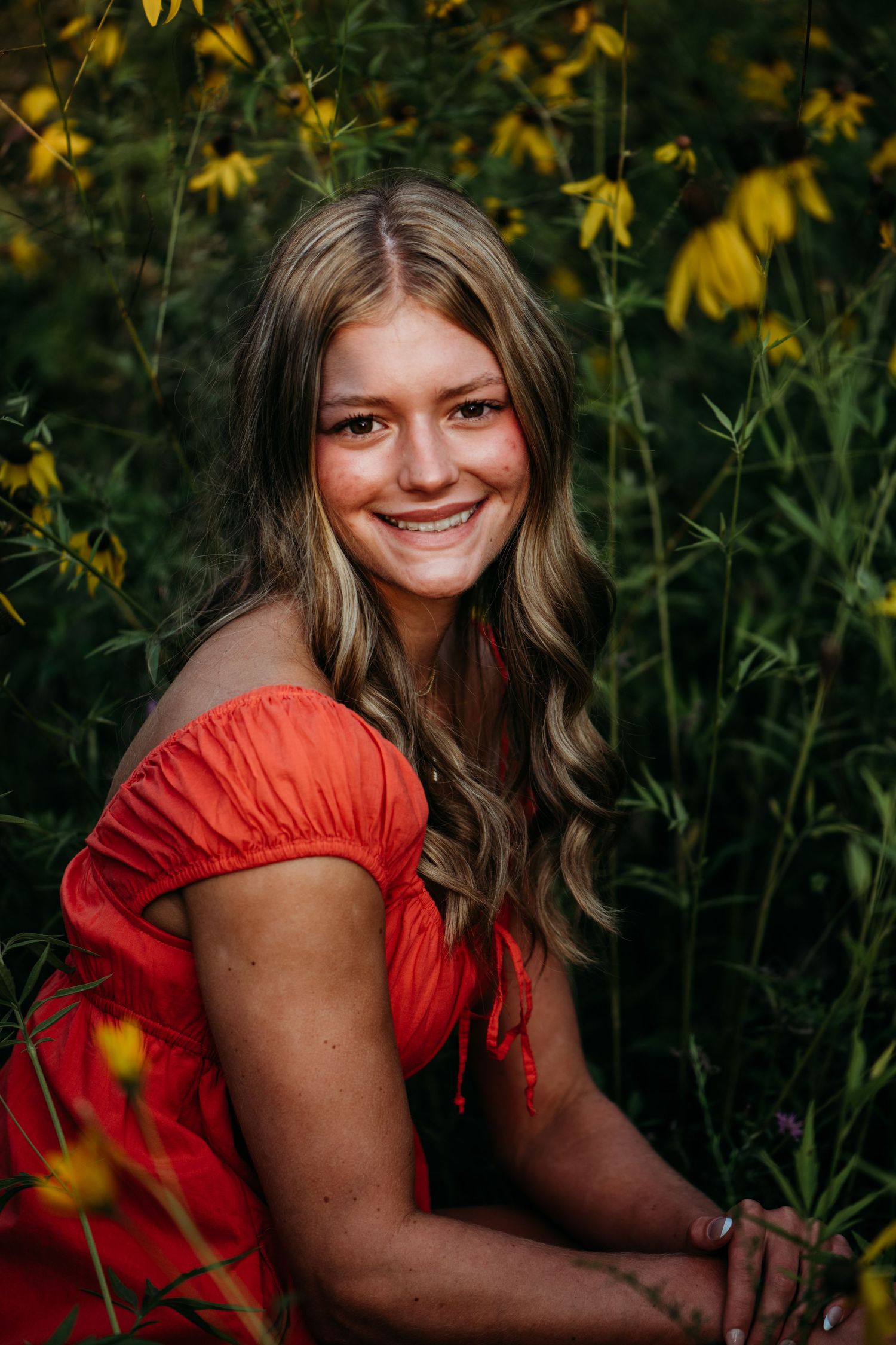 Portrait in a red dress sitting among vibrant yellow wildflowers on a summer evening.