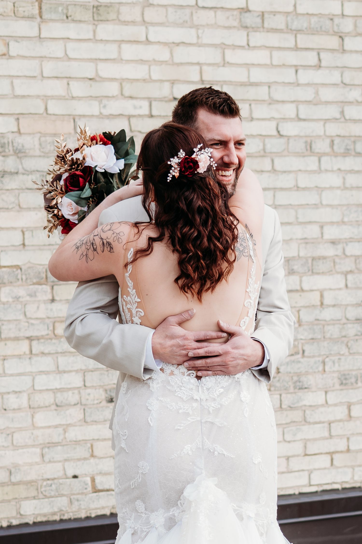 A tender embrace against a white brick wall with a floral wedding bouquet.