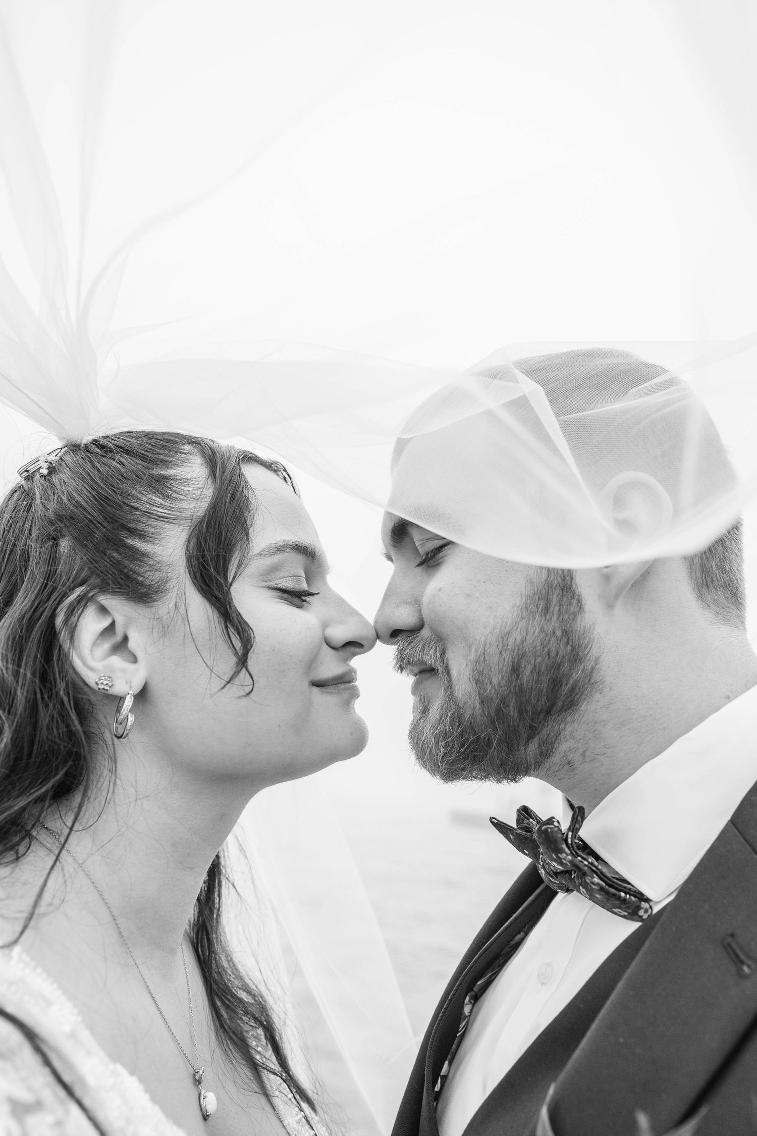 Black and white close-up of bride and groom sharing romantic moment under flowing veil.