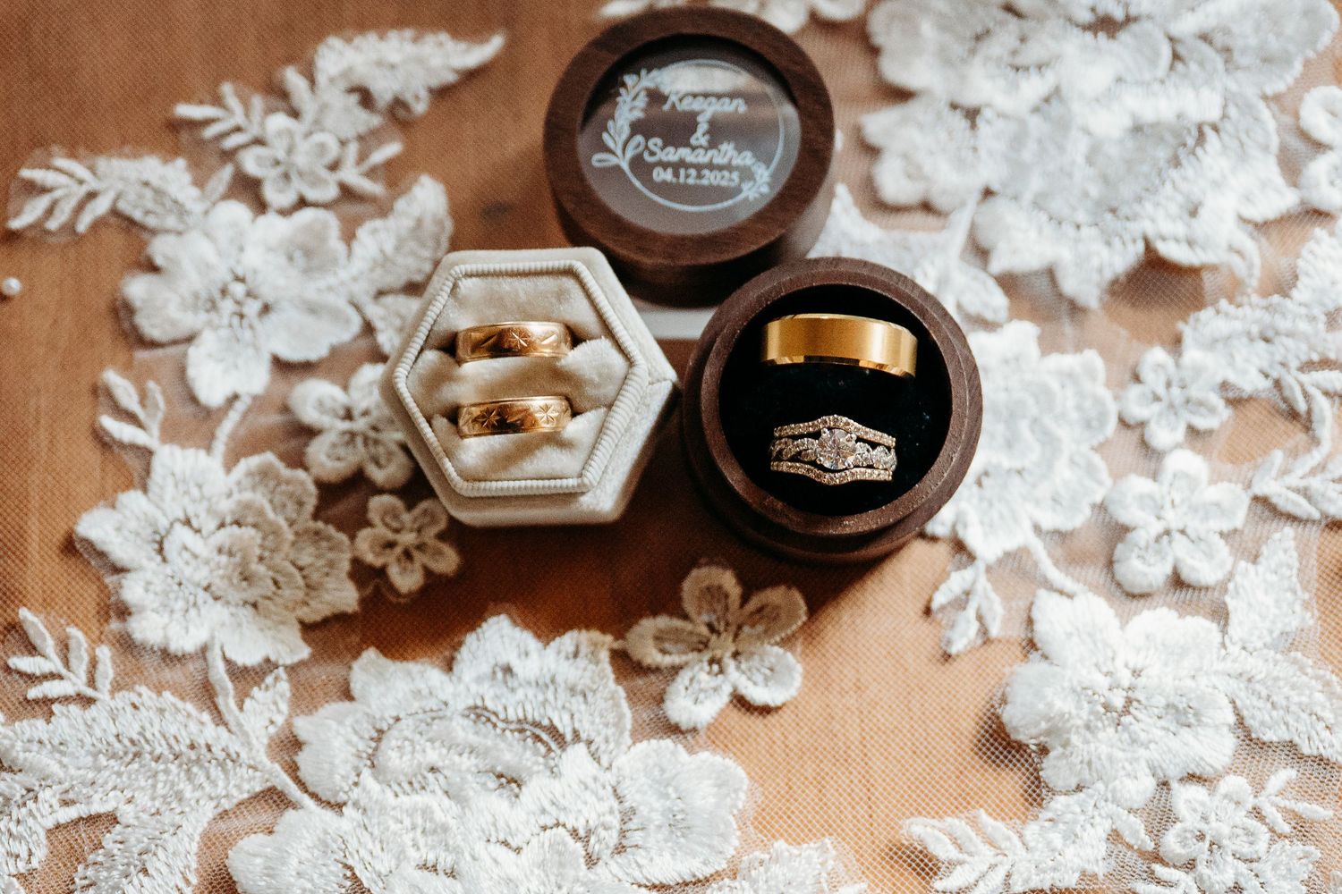 Two black ring boxes surrounded by delicate white lace flowers and petals on a wooden surface.