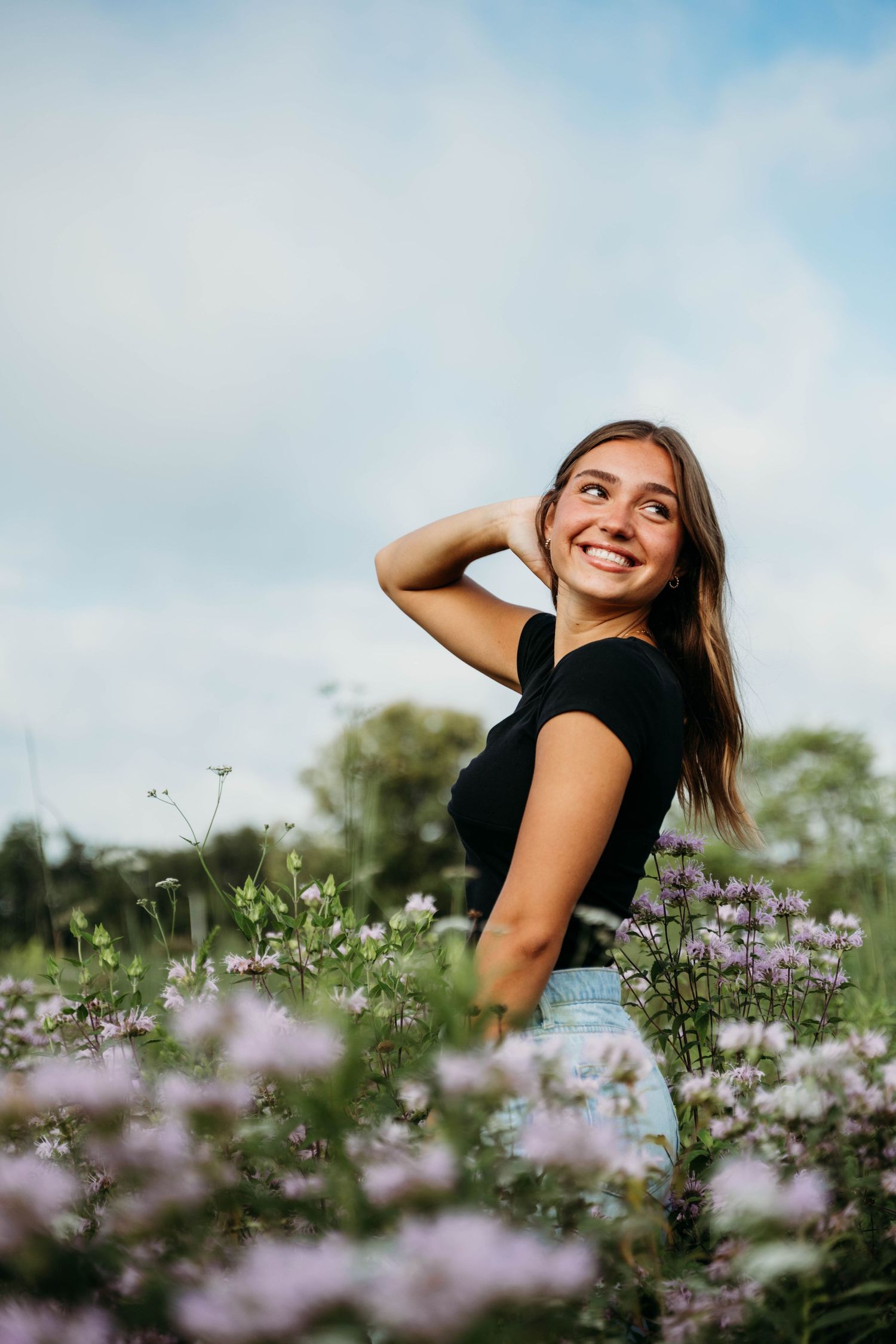 A joyful expression fills this candid summer portrait amidst a field of purple wildflowers.