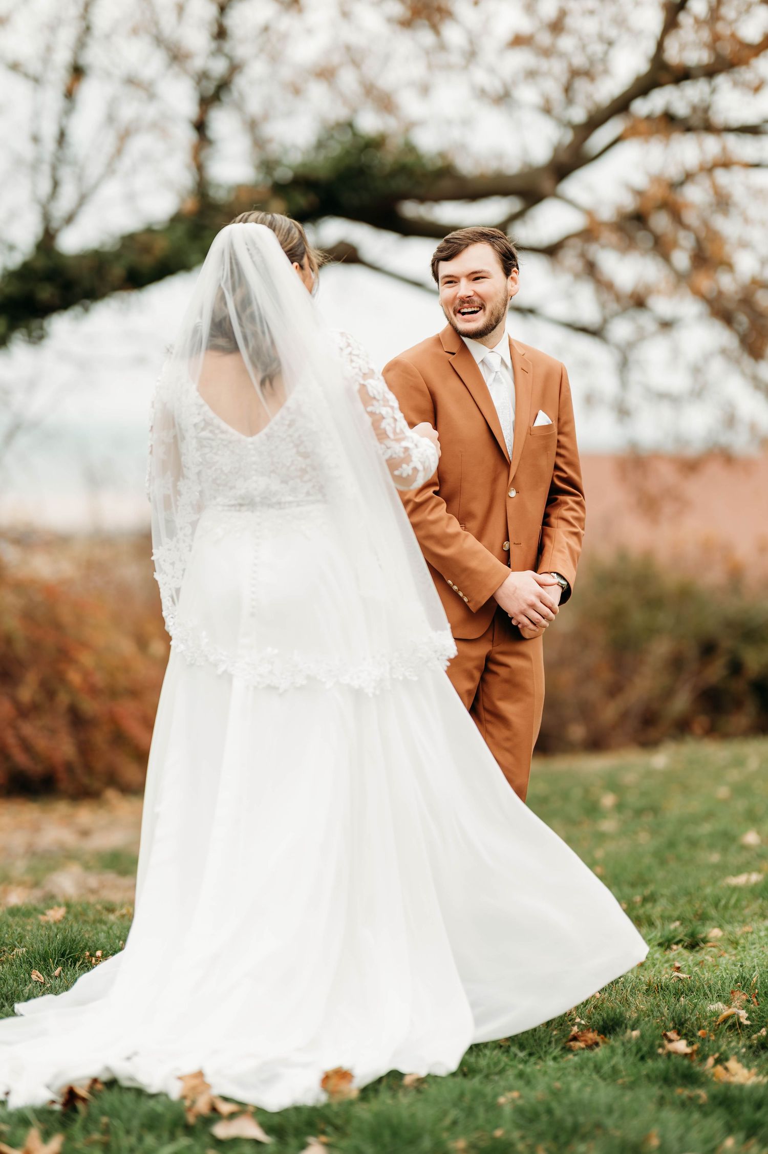 A bride and groom share a playful moment outdoors during an autumn wedding photoshoot with falling leaves.