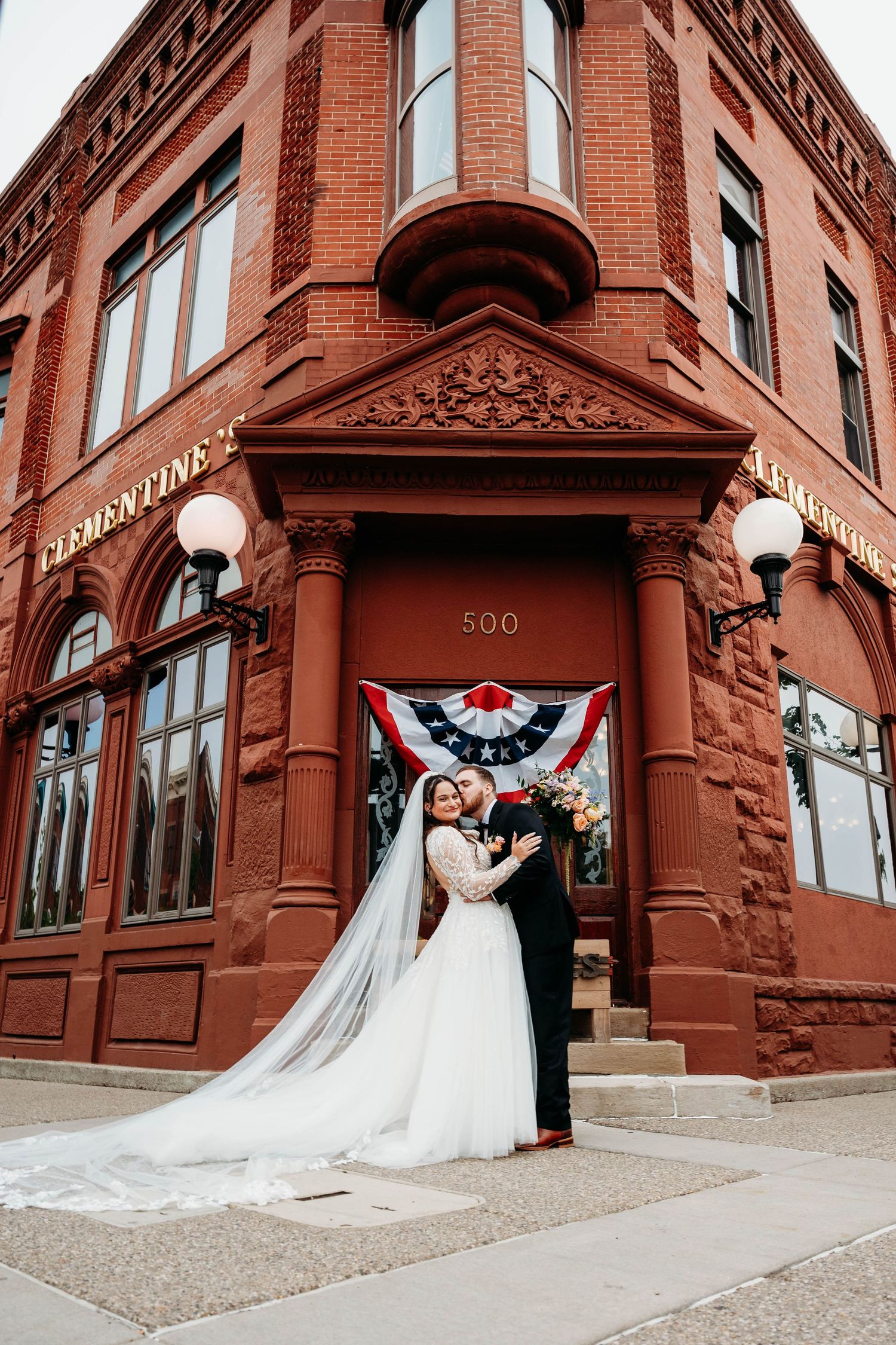 Bride and groom embracing in front of a historic red brick building at 500 Clementine.