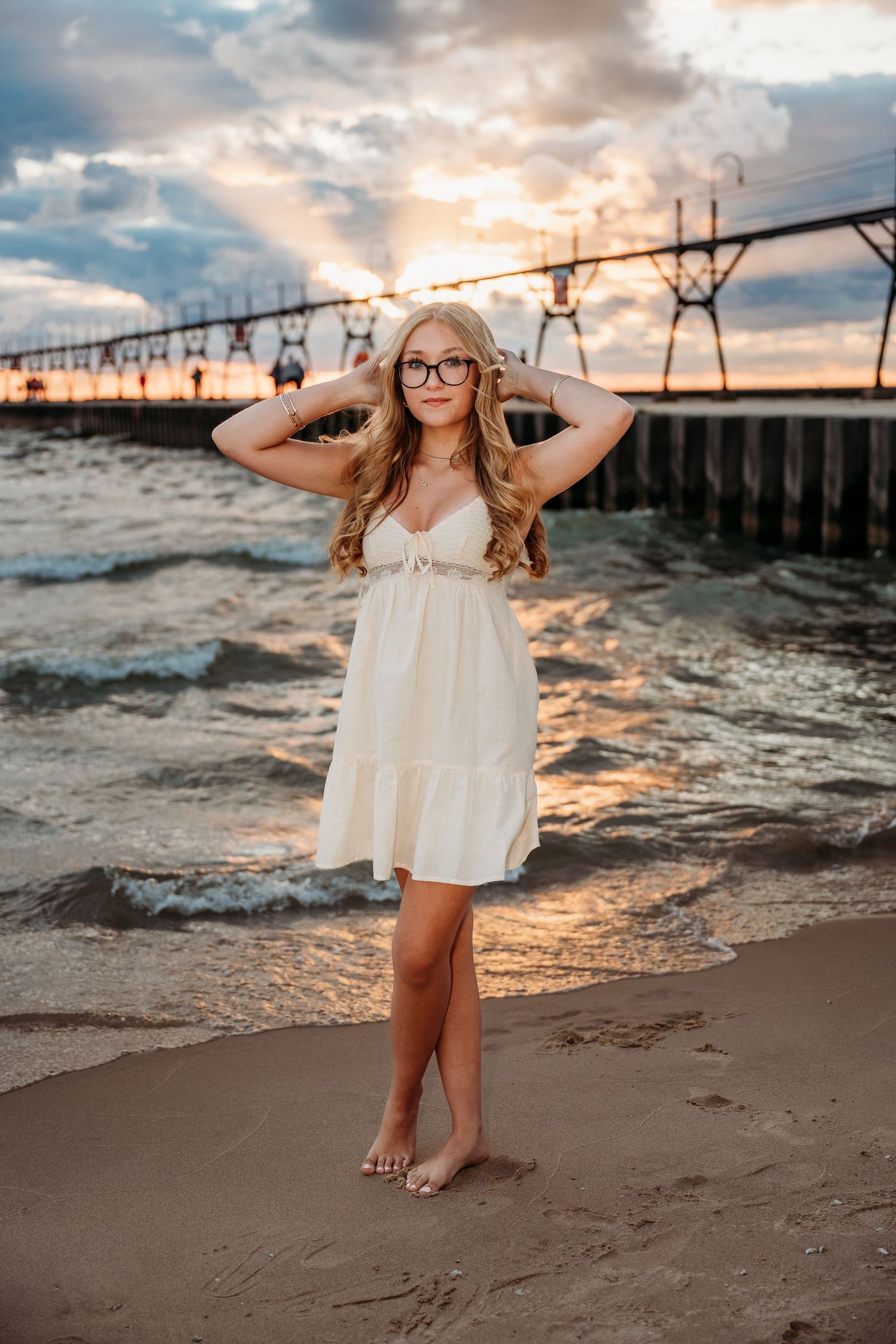 Sunset beach photography session showcasing a white dress against dramatic pier and ocean backdrop.