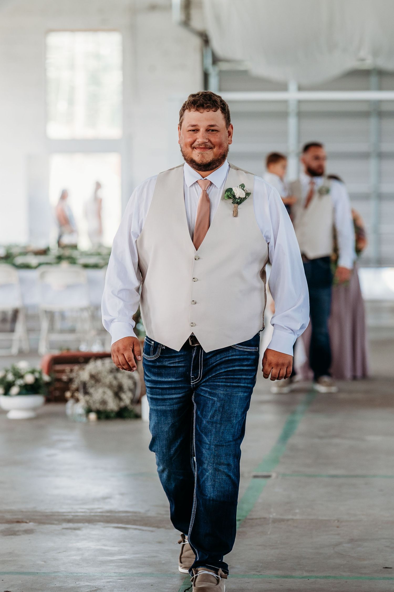 Wedding party member in white vest and jeans walking across an industrial indoor venue.