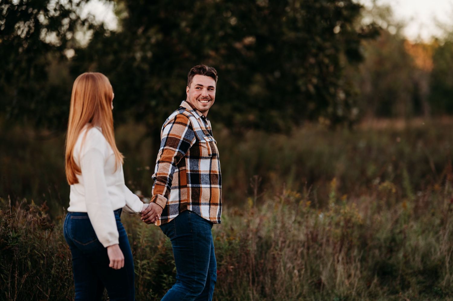 A couple walks through a golden autumn field at sunset holding hands and sharing intimate moments together.