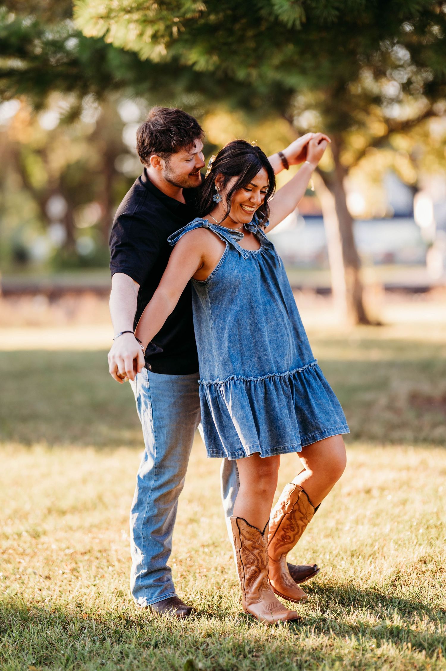 A couple in denim and boots walks together in a grassy park during golden hour.
