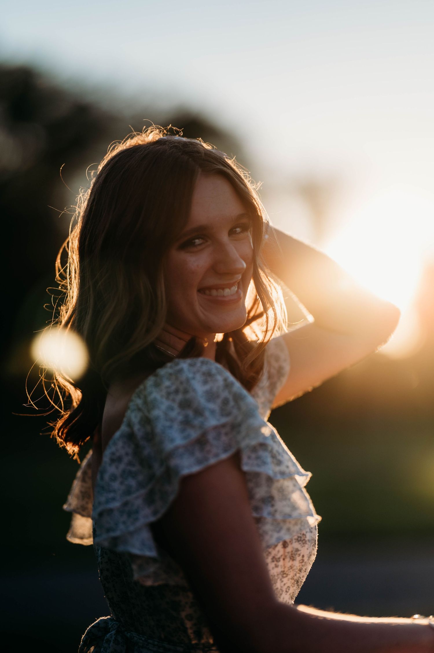 Woman in floral top smiling at golden hour sunset outdoors.