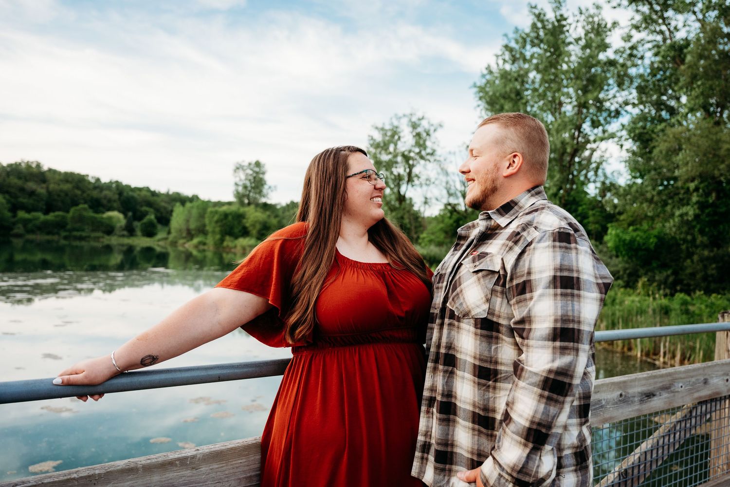 Couple in love sharing a romantic moment on a bridge overlooking a serene lake surrounded by lush green trees.