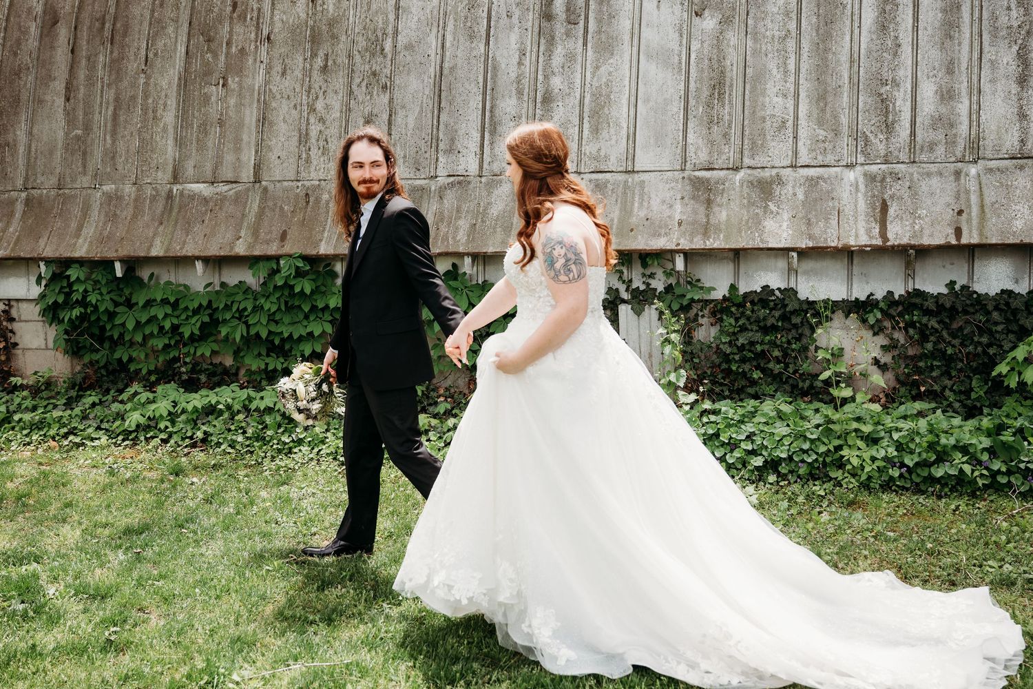 A couple shares their first look moment on their wedding day against a rustic barn wall and green foliage.
