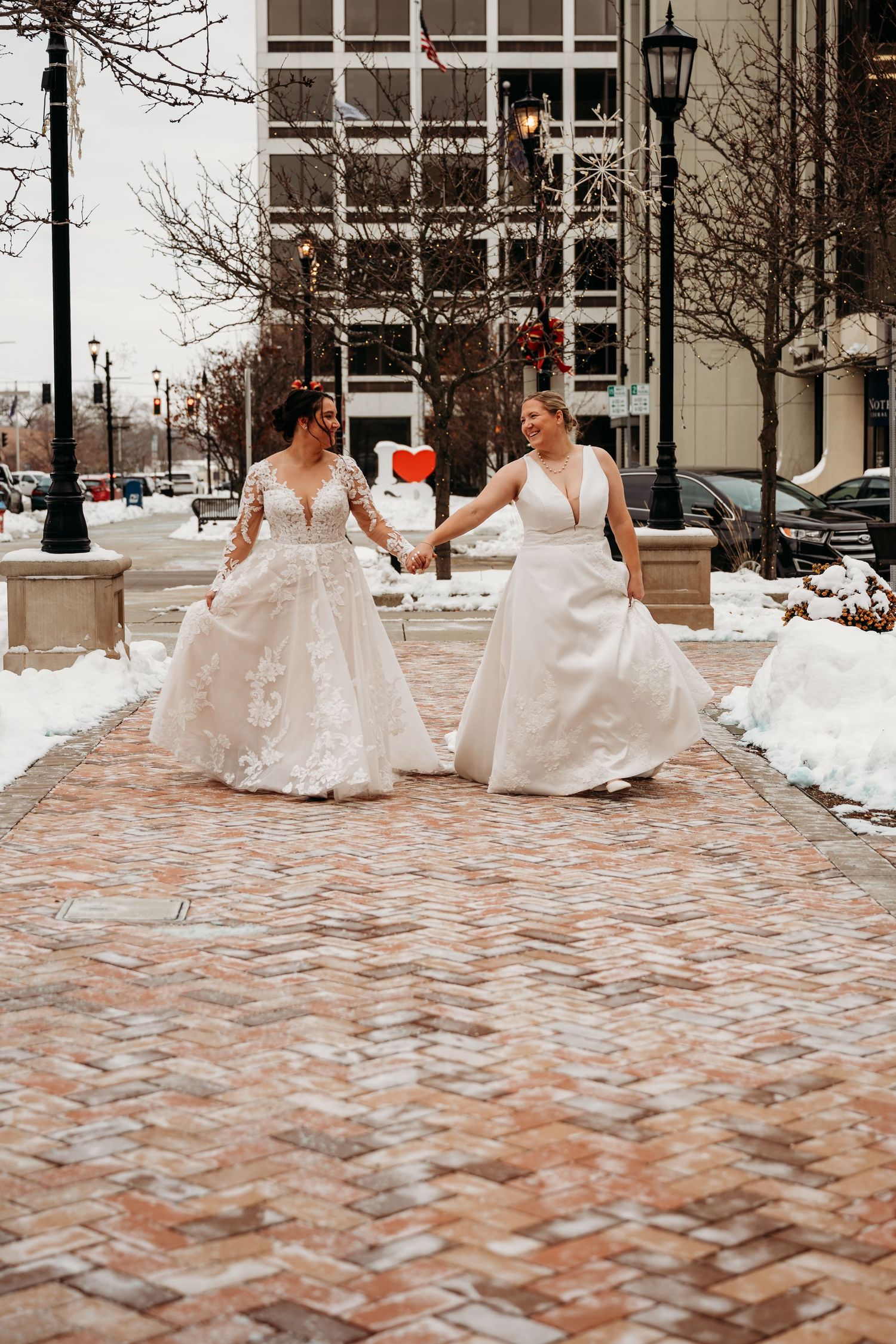 Wedding party in white dresses walking on snowy brick pathway during winter.