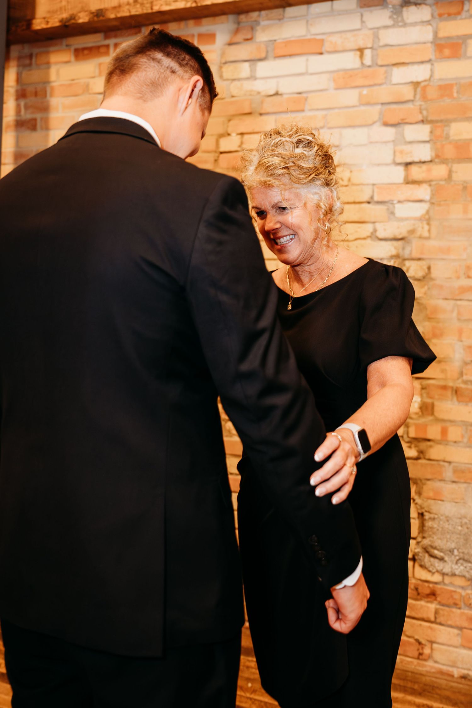 Two people in black clothing embrace against a brick wall in a candid emotional moment.