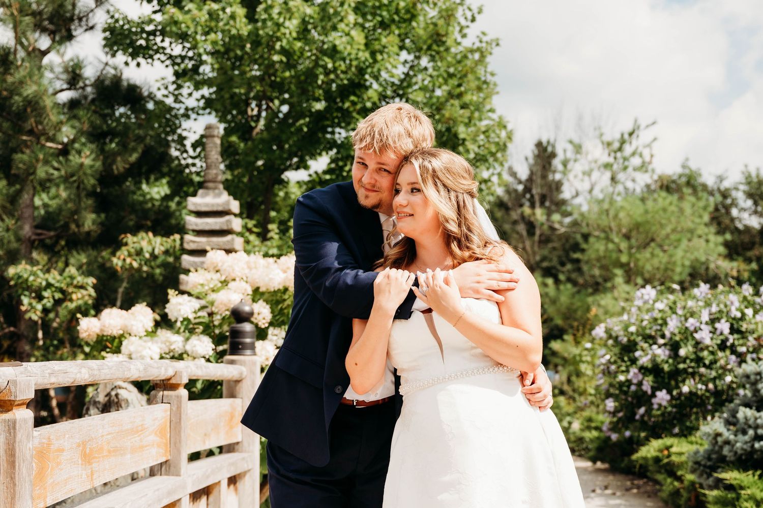 A joyful bride and groom embrace outdoors in a lush garden setting, sharing a happy moment on their wedding day.
