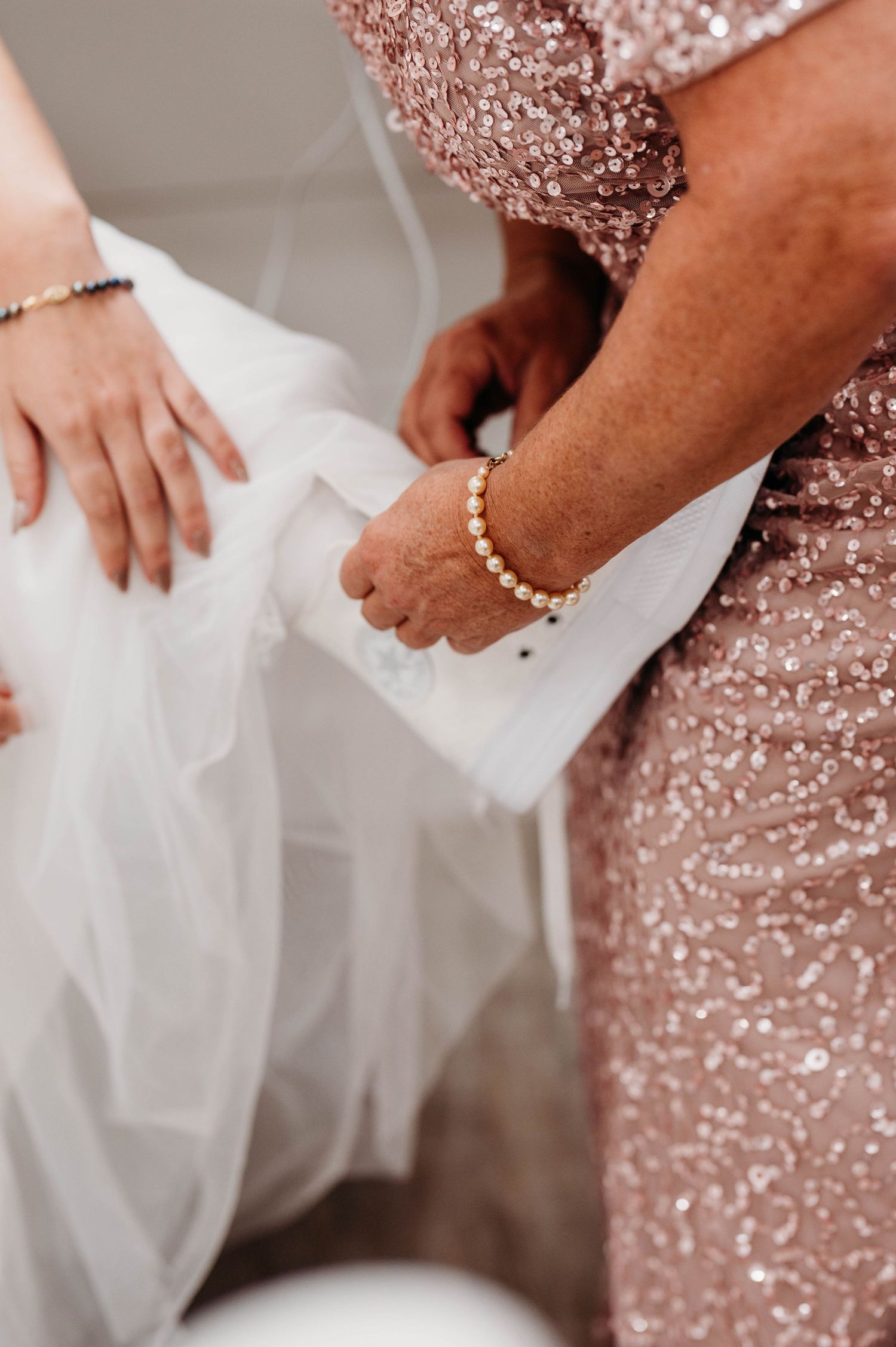 Close-up detail of hands adjusting a white wedding dress against a sparkly rose gold sequined dress.