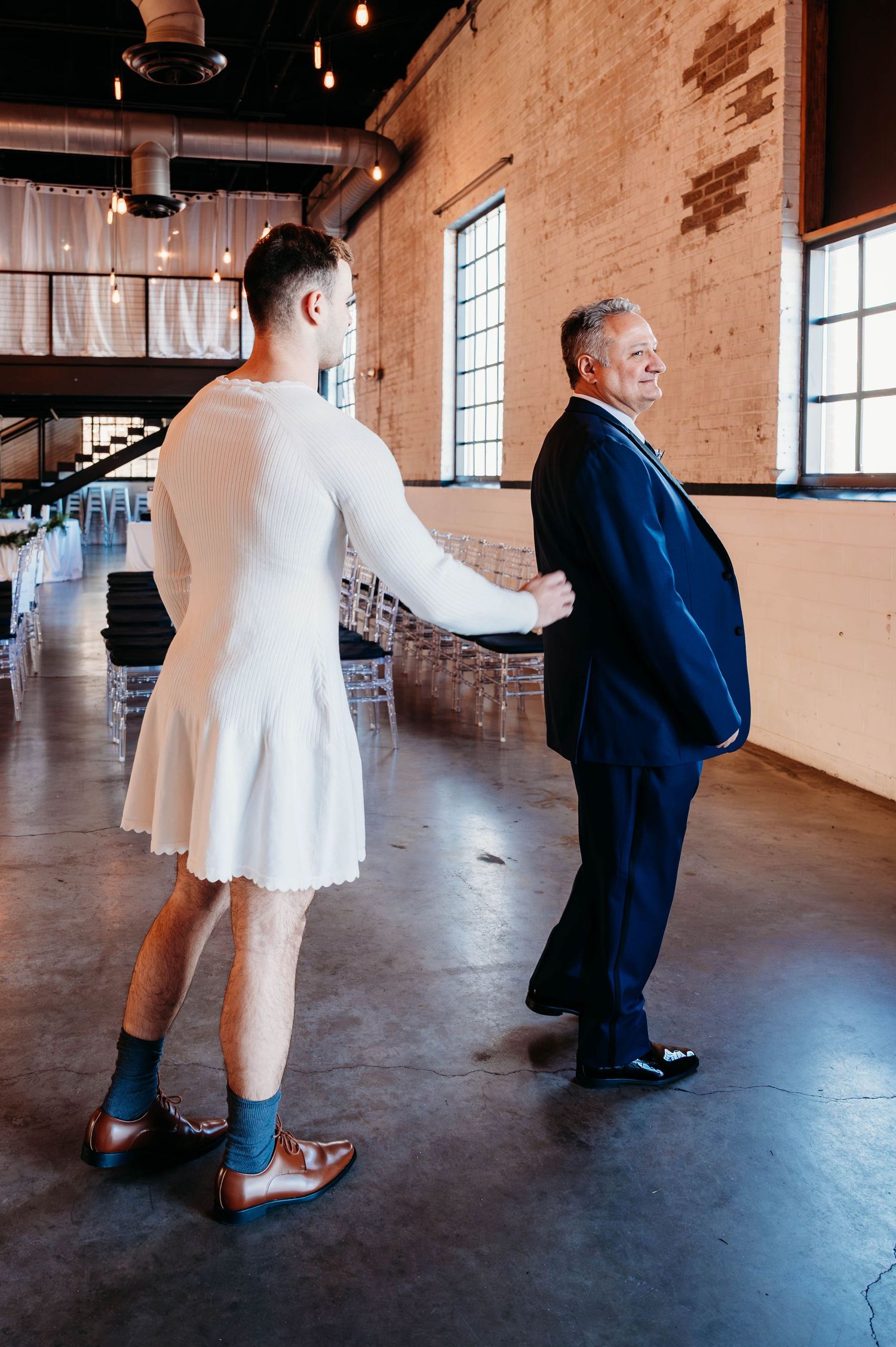 Two people share a first look moment in an industrial venue with brick walls and large windows.