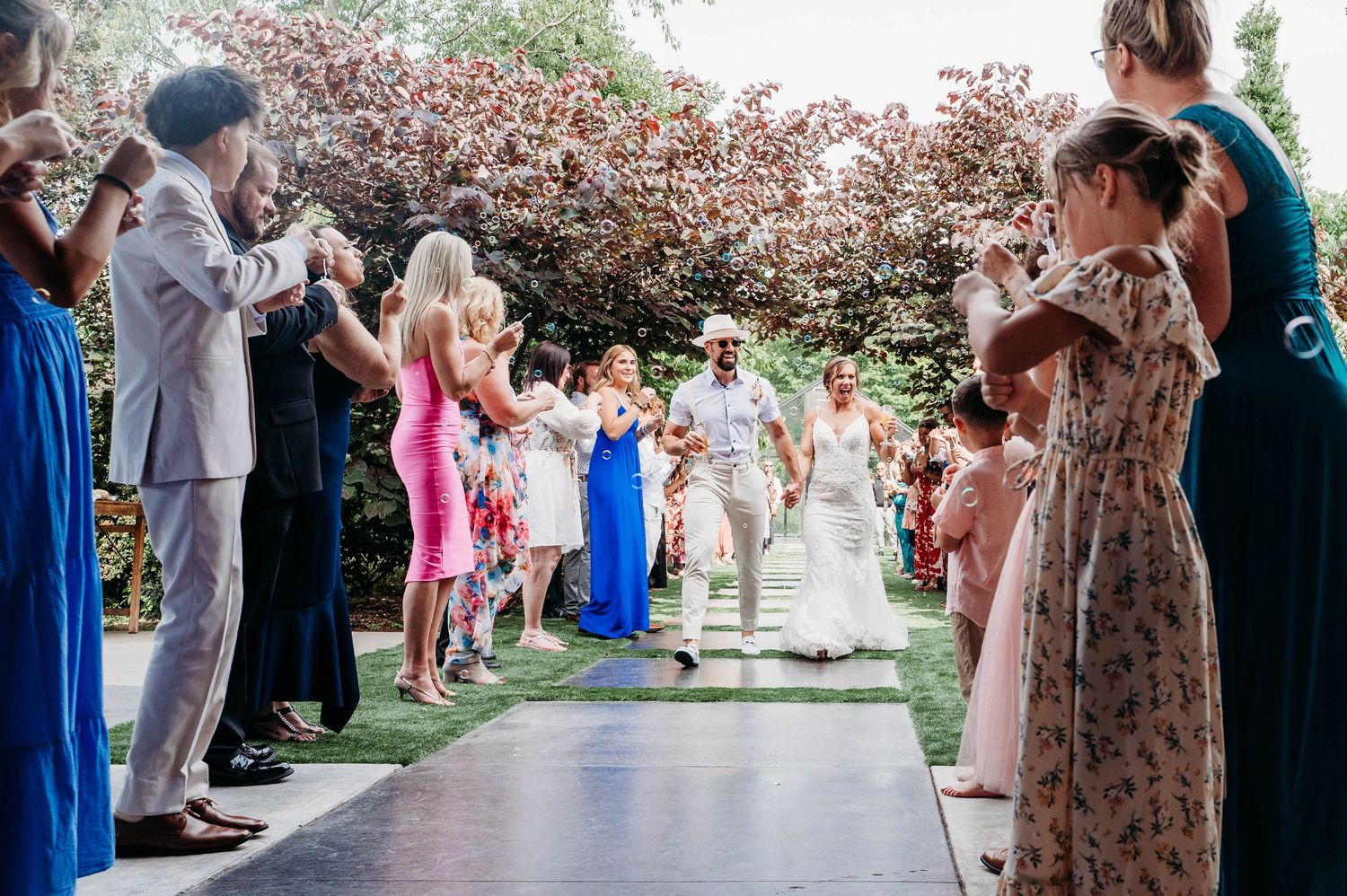 Wedding guests stand in line under blooming cherry trees during an outdoor spring ceremony.