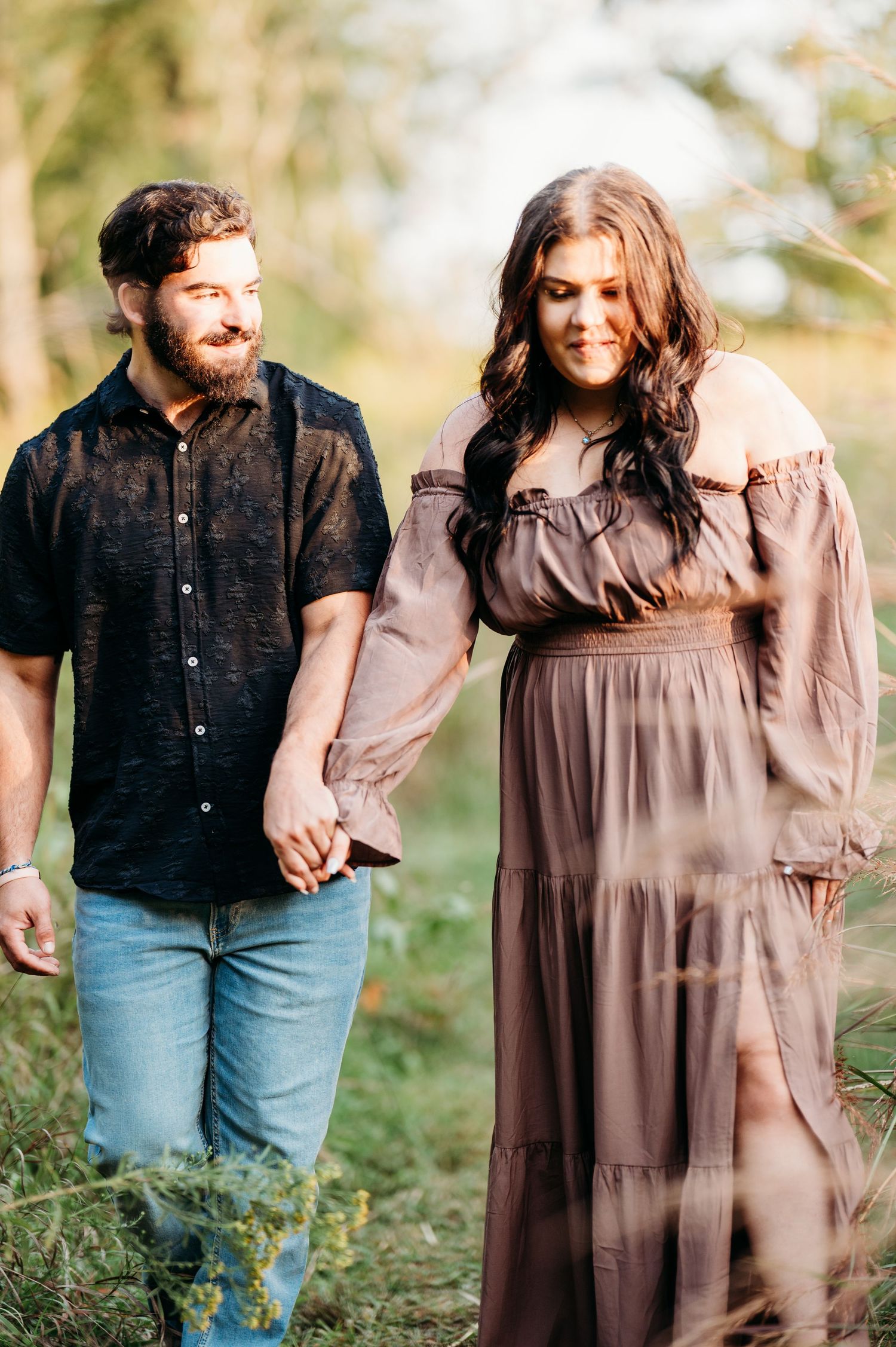 A couple in casual attire shares tender moments while walking together in a sunlit outdoor setting.