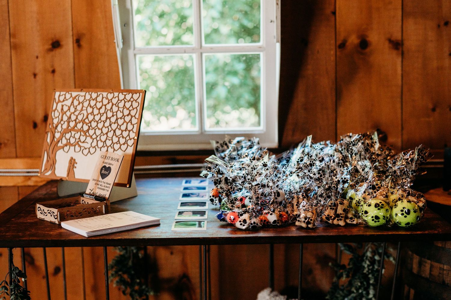 A wooden book stand with decorative patterns sits on a rustic table beside dried flowers near a bright window.