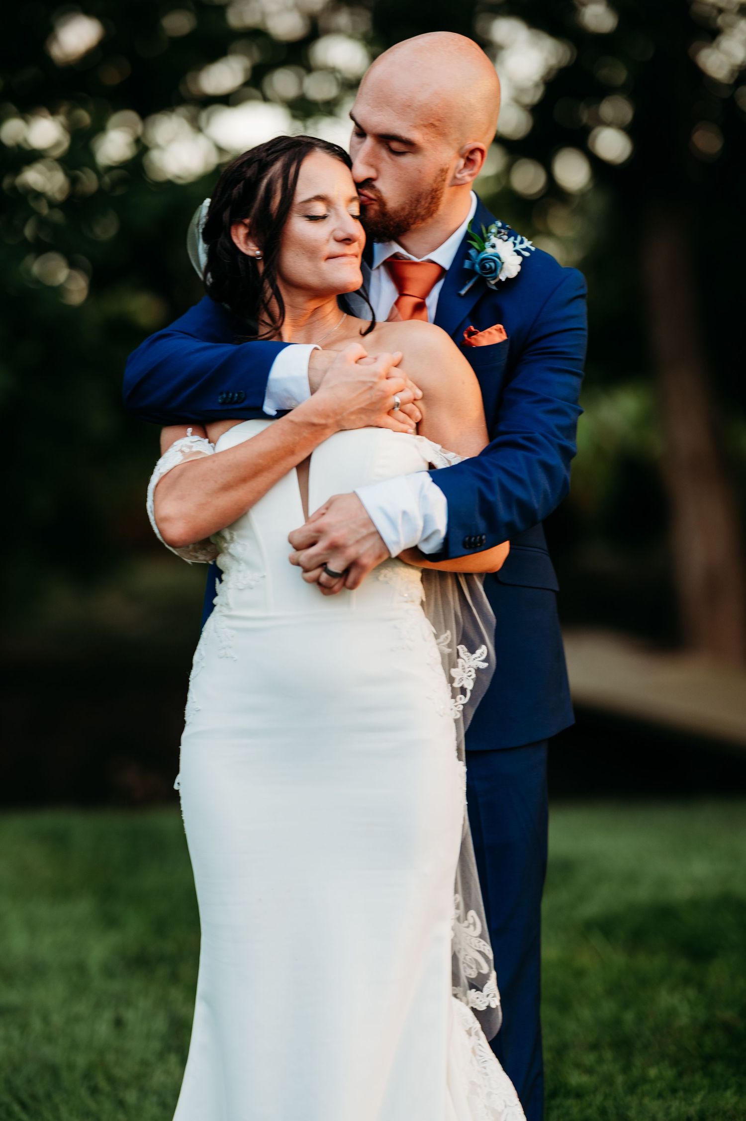 Romantic wedding couple embraces in a garden setting with soft bokeh lighting in the background.