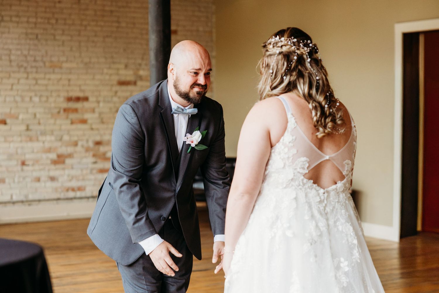 A couple shares a joyful moment dancing together in a rustic brick-walled venue during their wedding celebration.