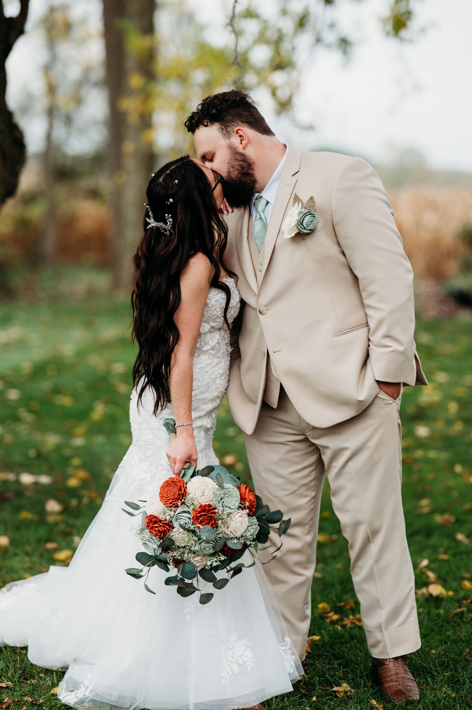 Romantic wedding couple shares intimate moments in autumn garden with white dress and tan suit against fallen leaves.