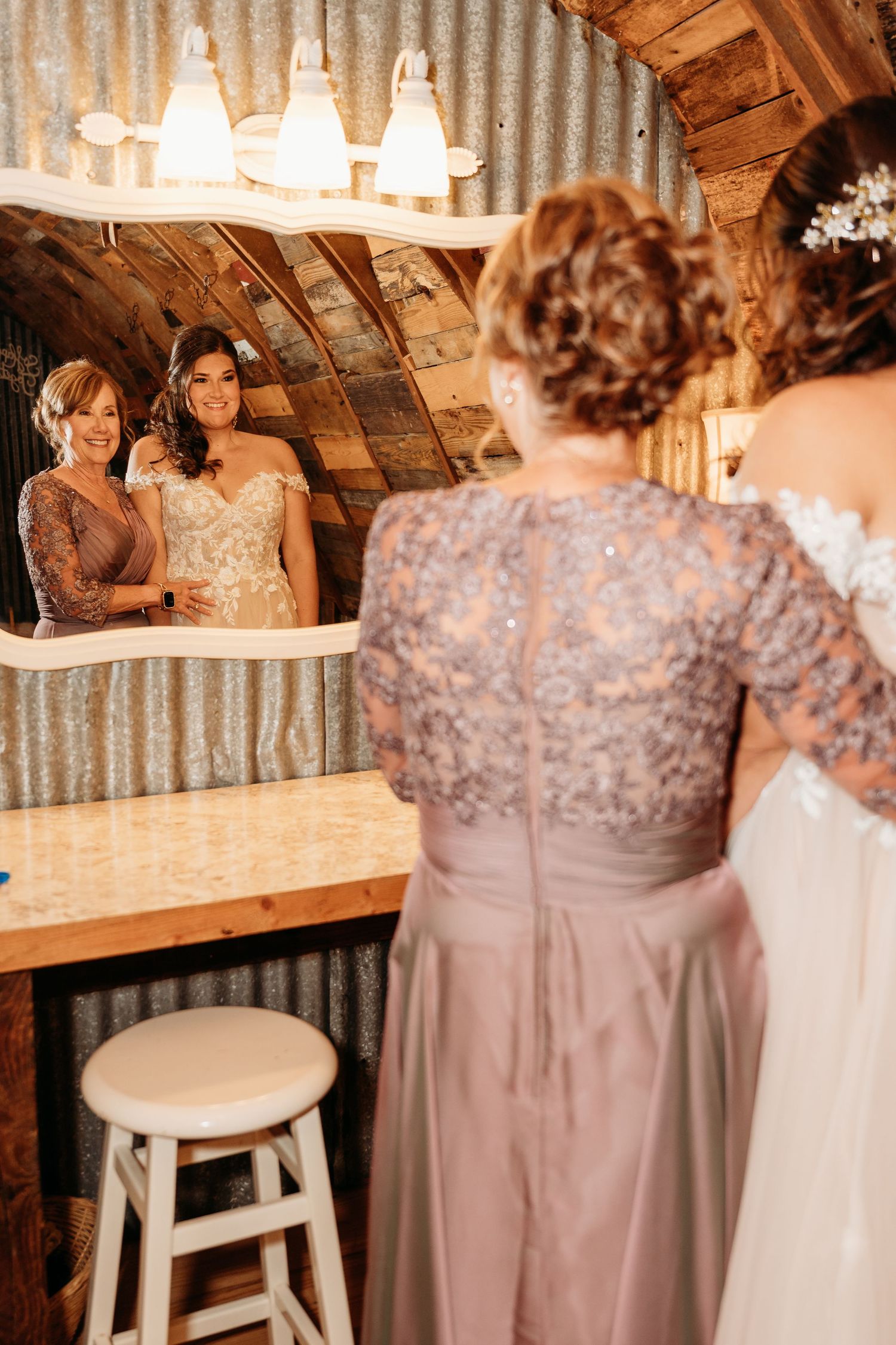Bridesmaids in mauve dresses gather around a rustic wooden bar during wedding reception.