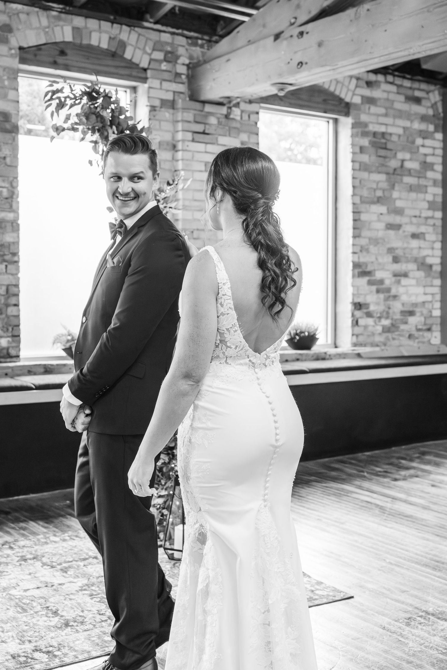 An emotional first look moment captured between a couple in formal wedding attire in a rustic brick-walled venue.