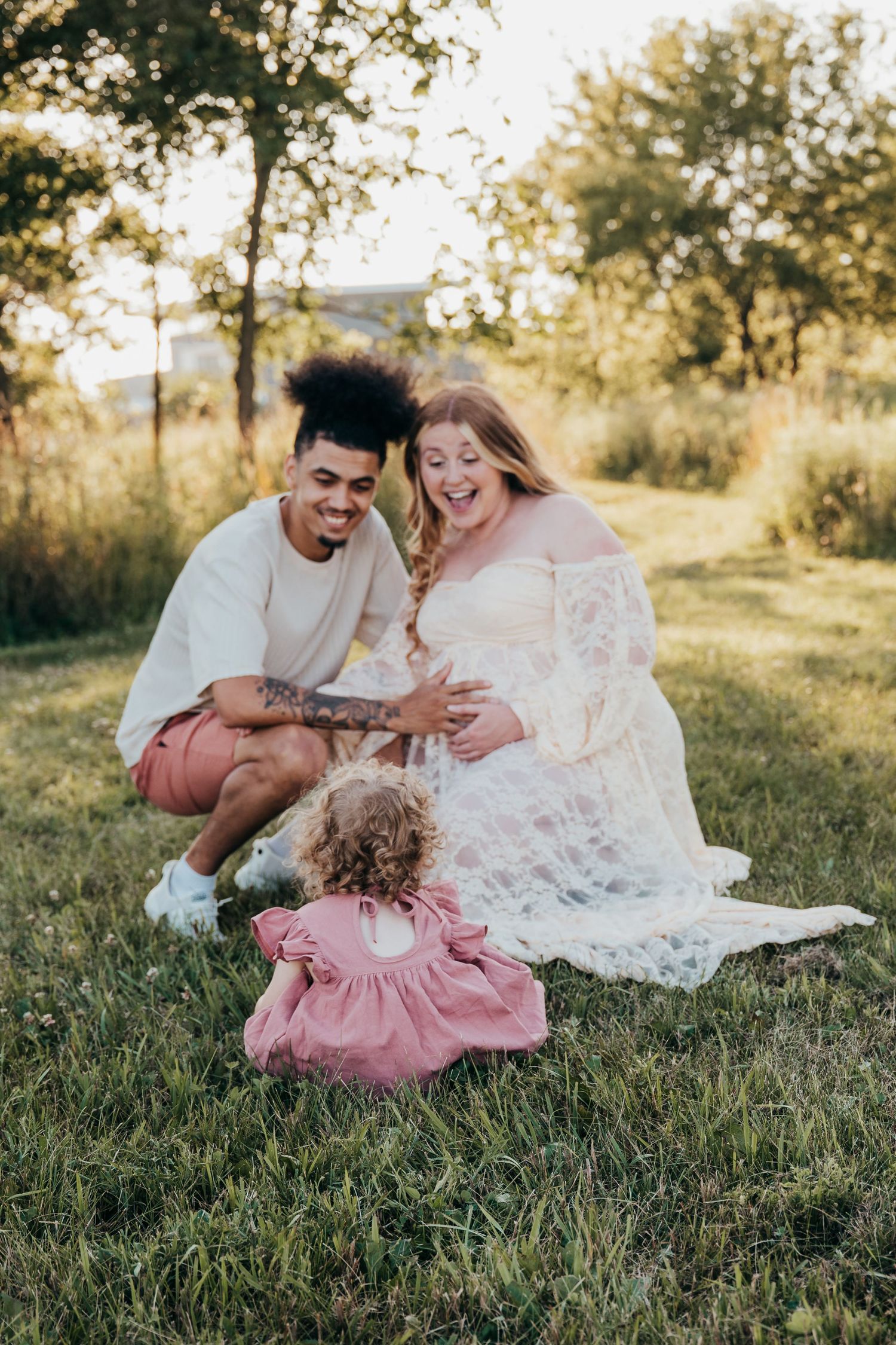 A joyful family moment captured outdoors during a maternity photoshoot with matching pink and white outfits.