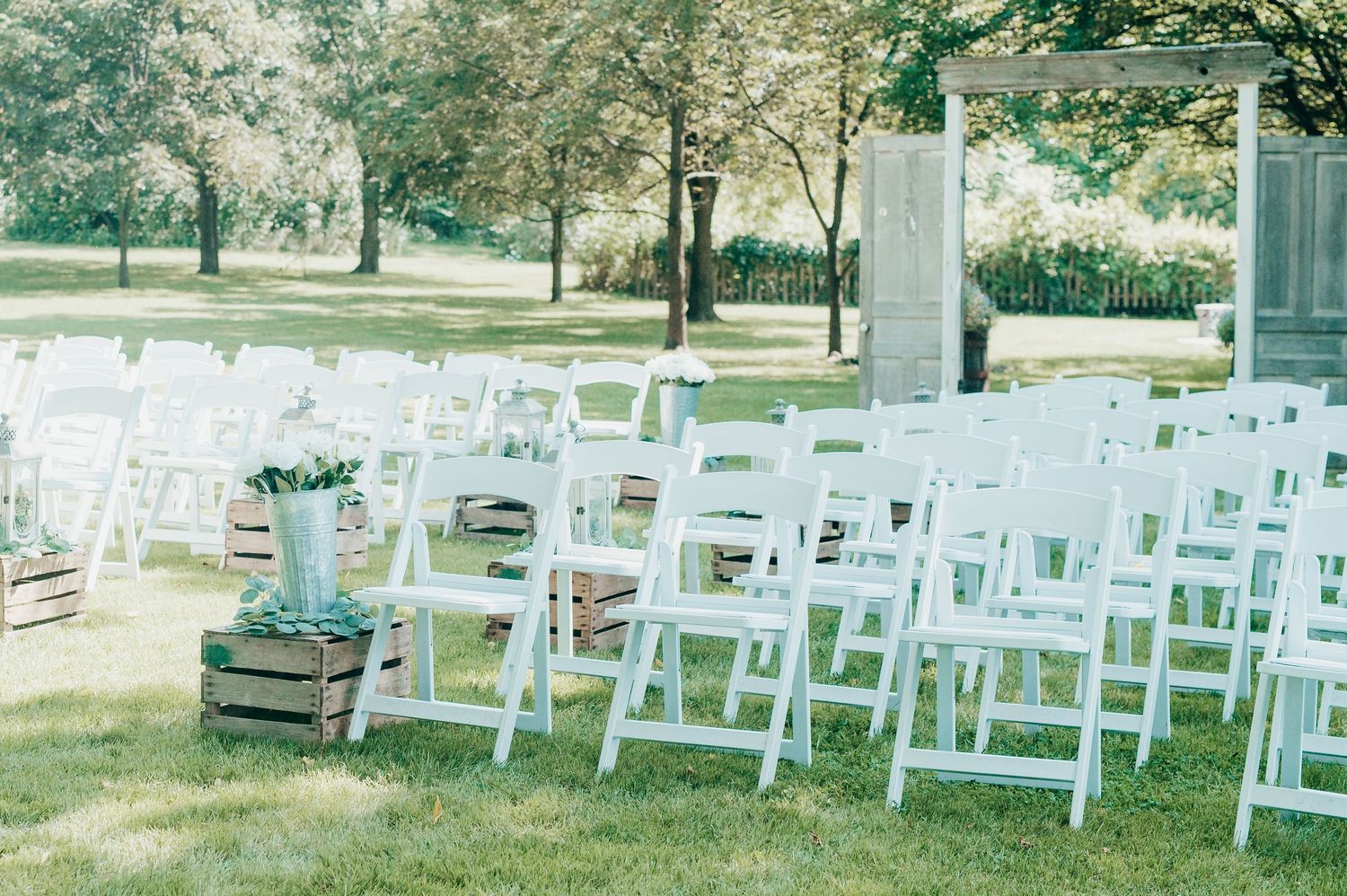 White wooden folding chairs arranged in rows on a grassy lawn for an outdoor wedding ceremony.