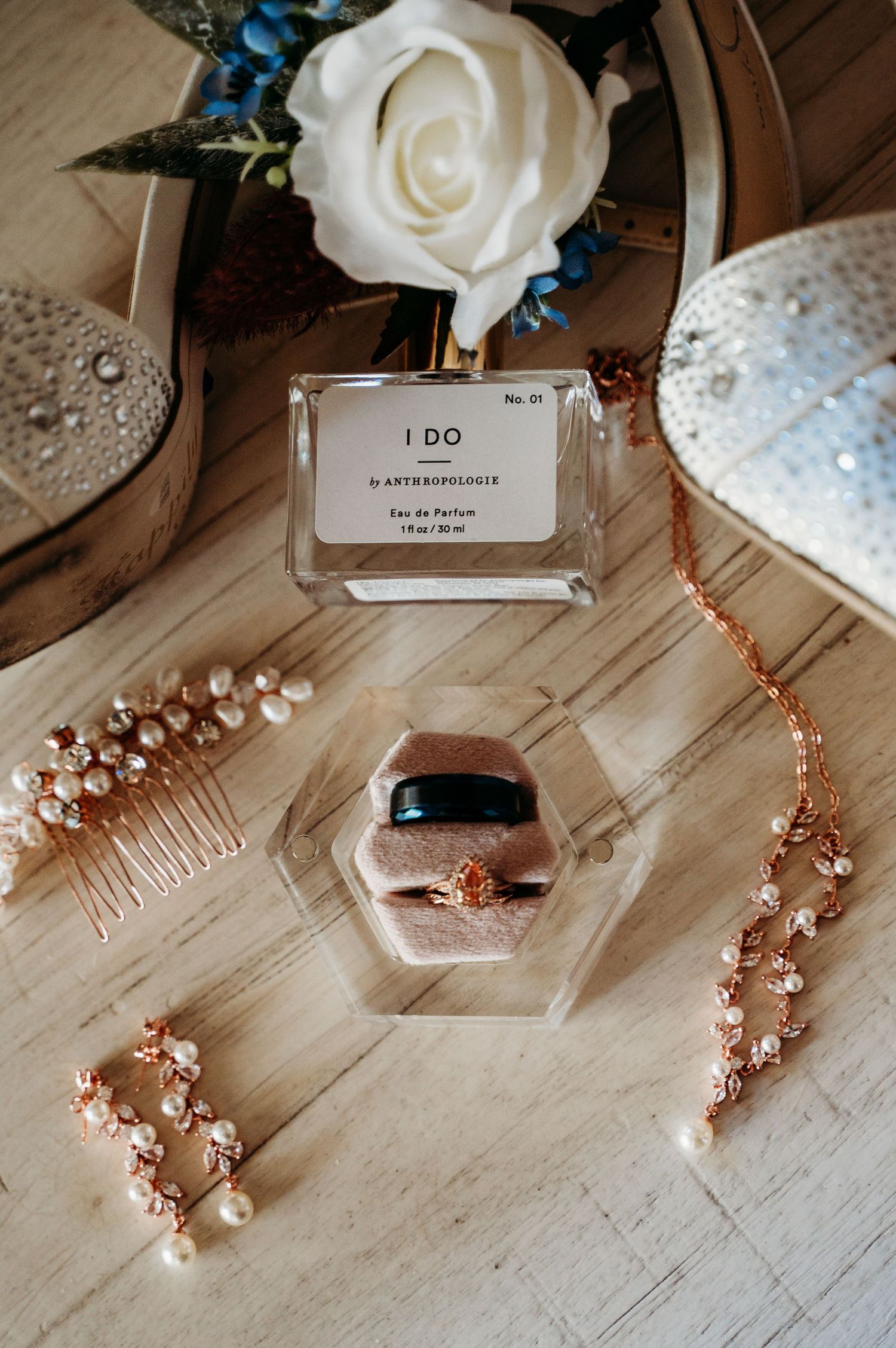 Wedding accessories including perfume, jewelry, and white rose on wooden surface.