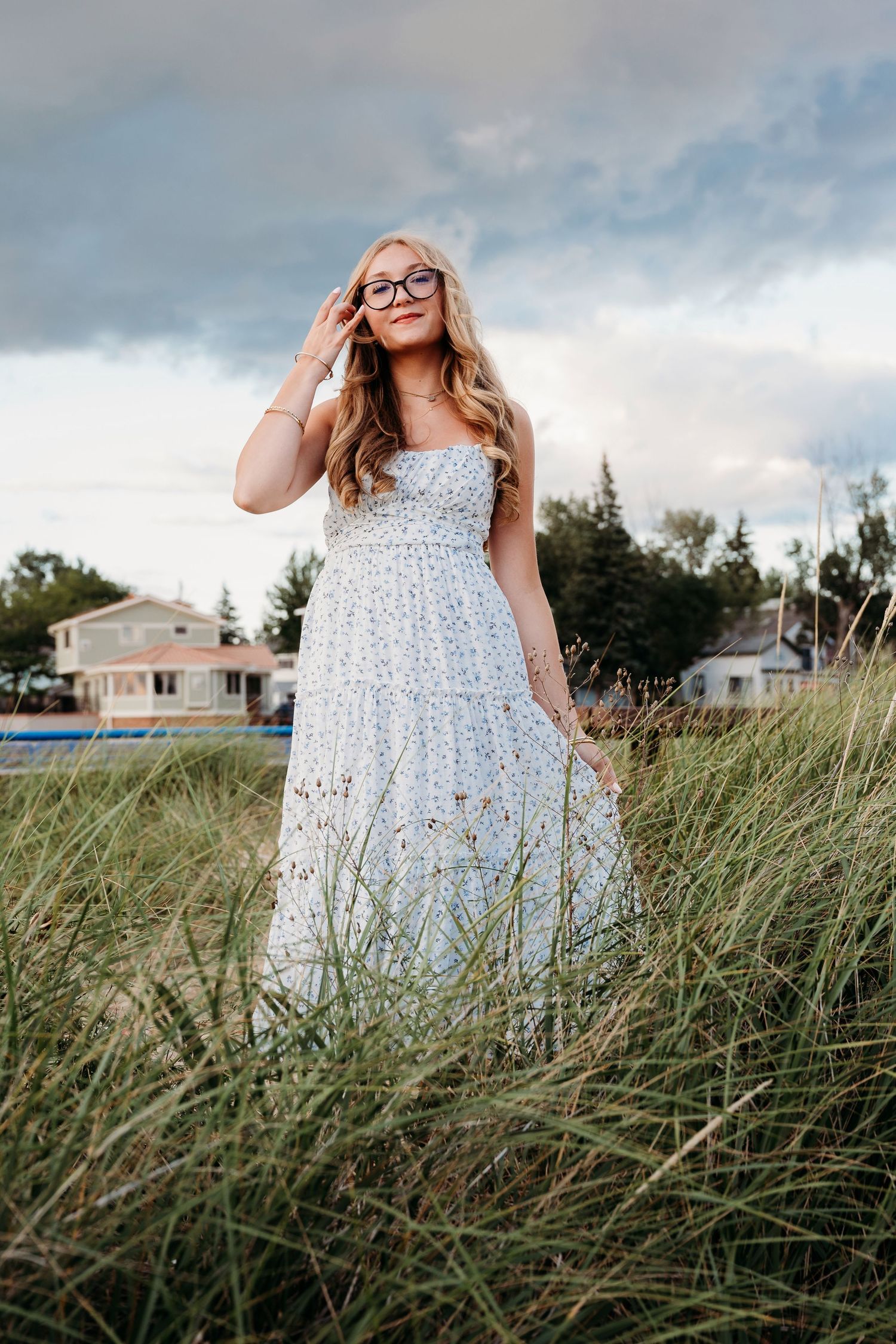 Person in a floral summer dress poses in tall beach grass against a cloudy sky.